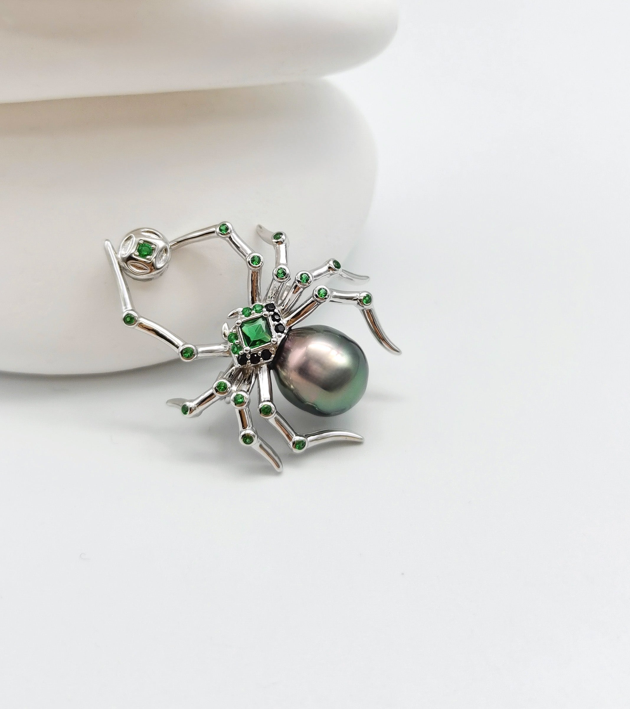 a spider brooch with large Tahitian baroque pearl sitting on white stones with starfish background