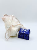 FRESHWATER WHITE PURPLE TWIN STRAND draped over a large conch with a blue ceramic house