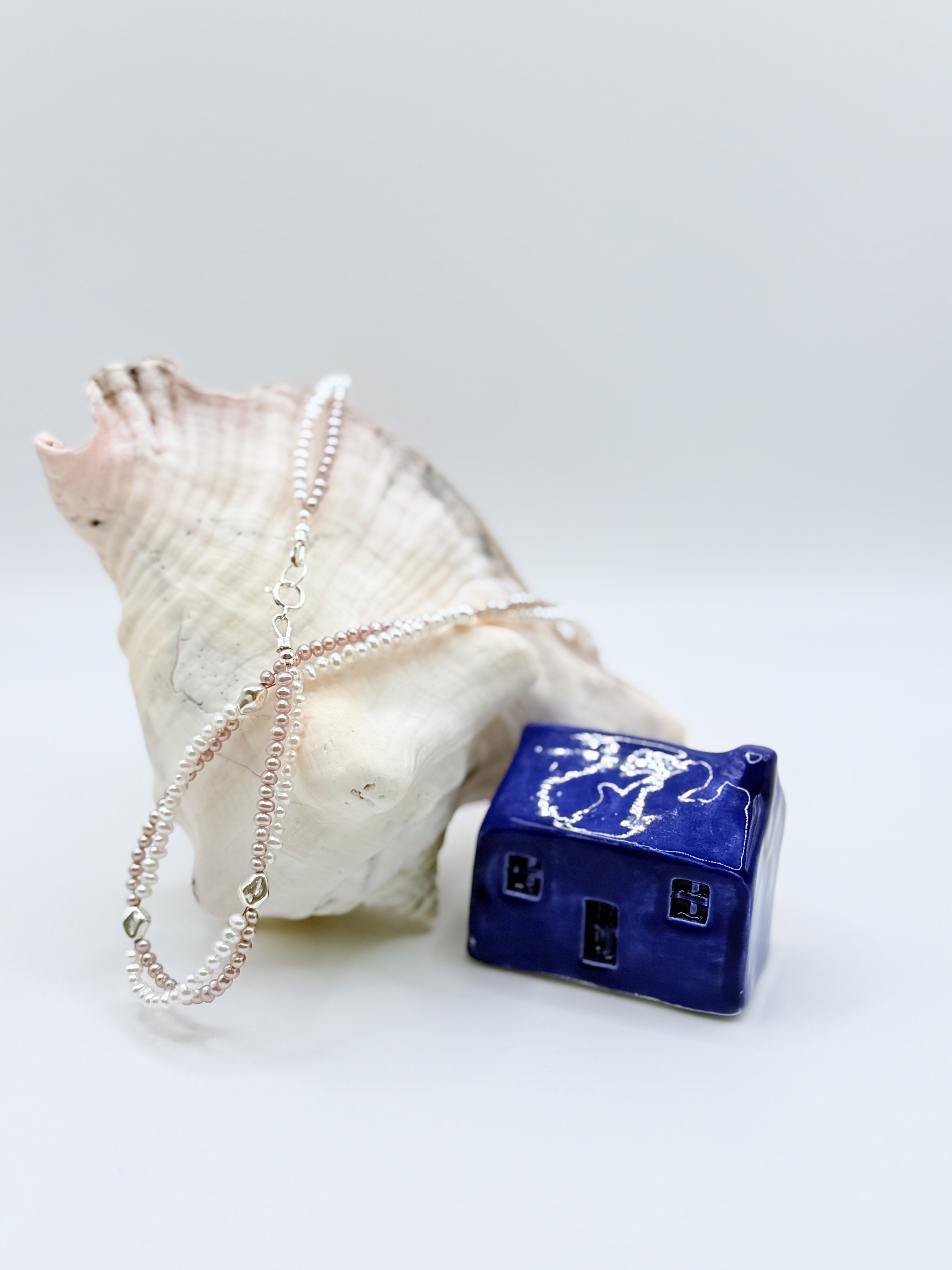 FRESHWATER WHITE PURPLE TWIN STRAND draped over a large conch with a blue ceramic house