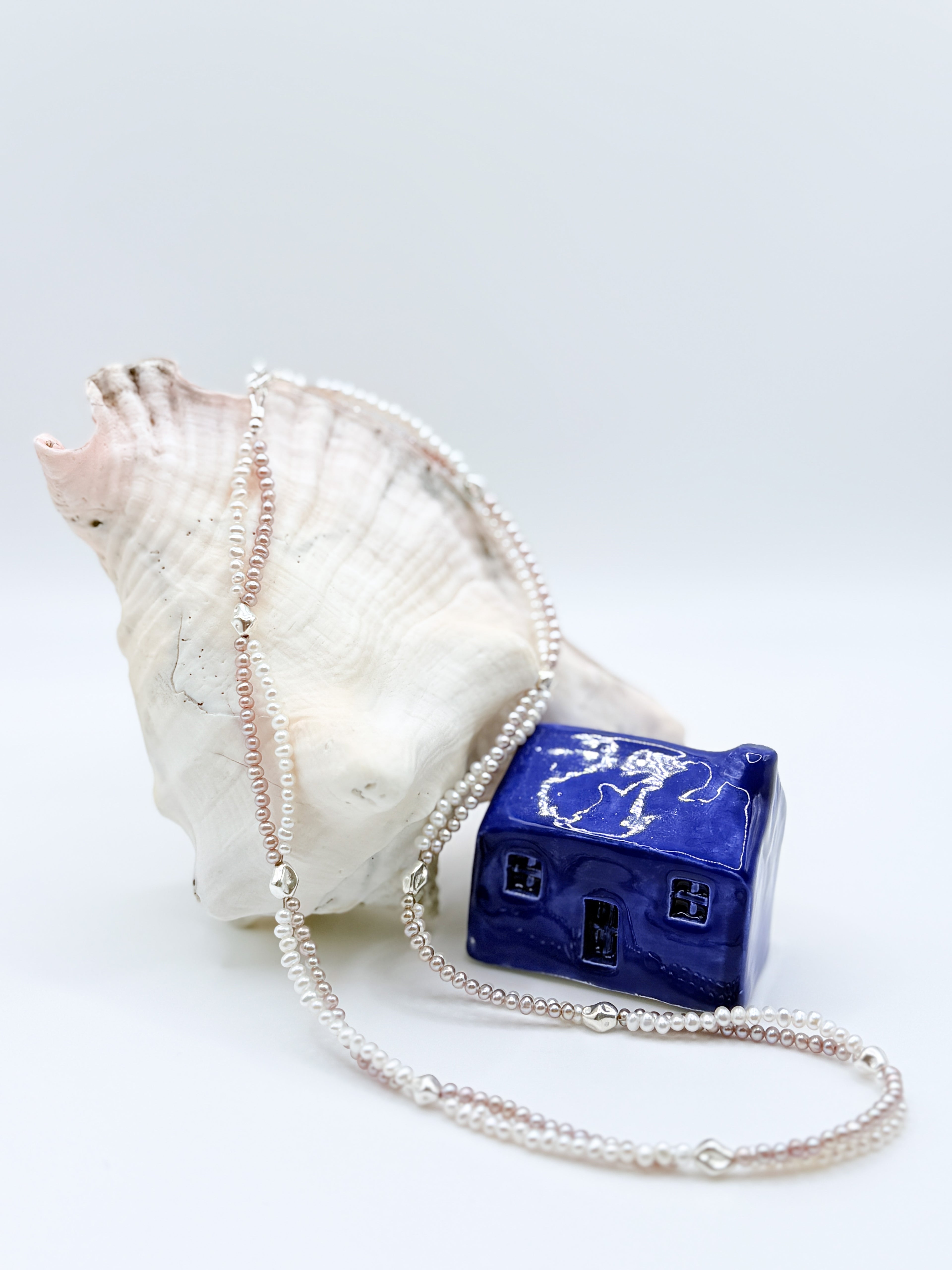 FRESHWATER WHITE PURPLE TWIN STRAND draped over a conch in a natural flow