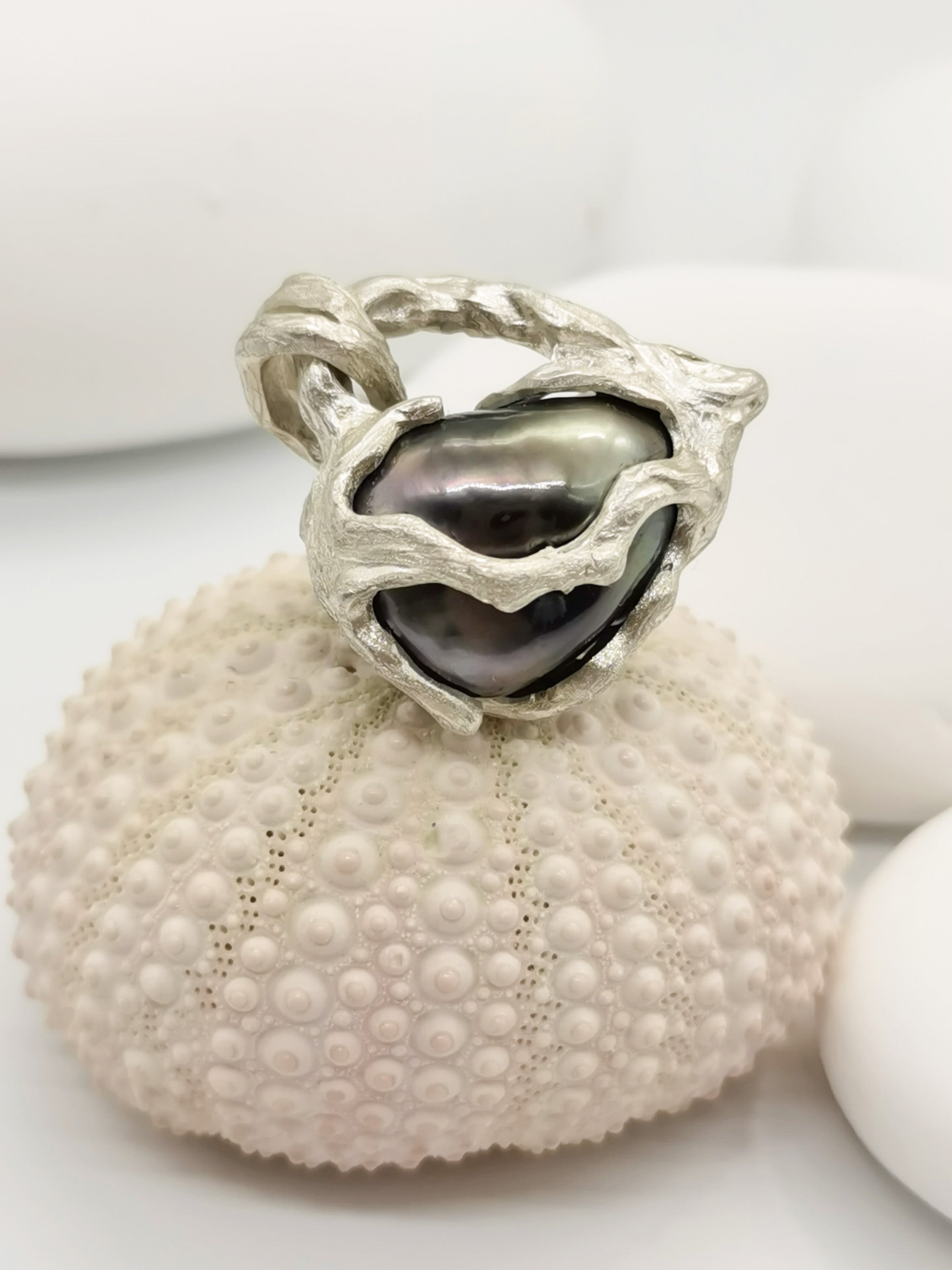 TAHITIAN PEARL HEART PENDANT placed on top of a sea shell showing open back details of the silver work and lustre of the pearl 