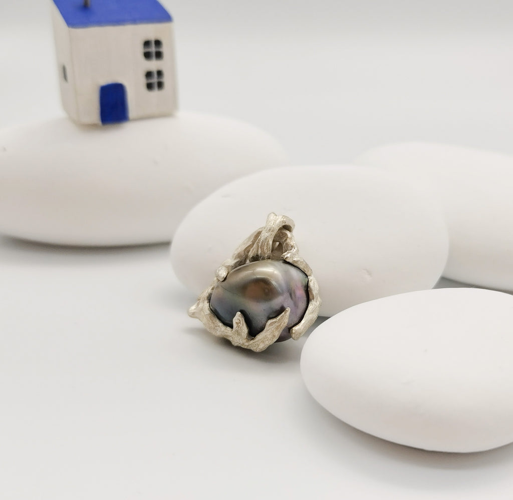 The Tahitian Pearl heart pendant resting against white stone with a little house in the background 