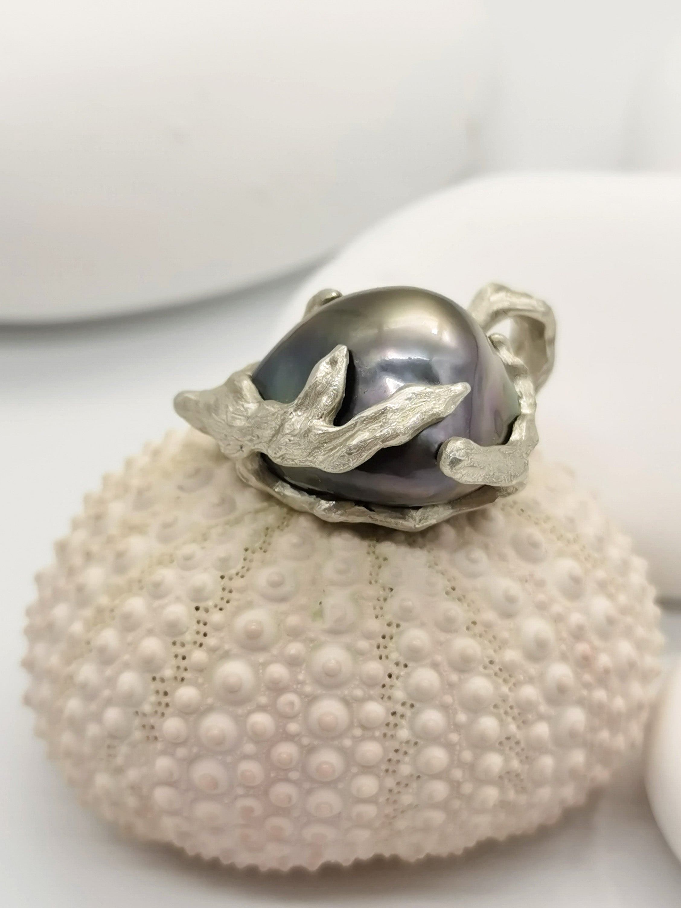 Closed-up side view of the Tahitian pearl heart pendant sitting on top of a seashell 