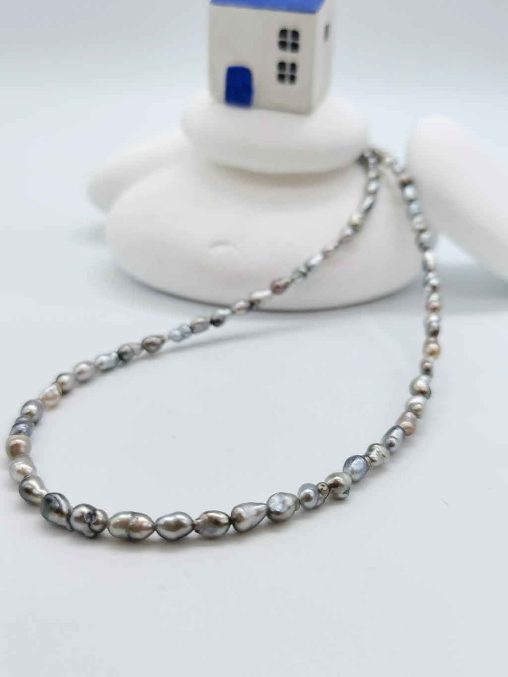 CLOSE UP VIEW OF THIRD PAIRNING NECKLACE OPTION FOR BAROQUE SUNBURST PENDANT, lay flat on white background with white stones and little house in the background
