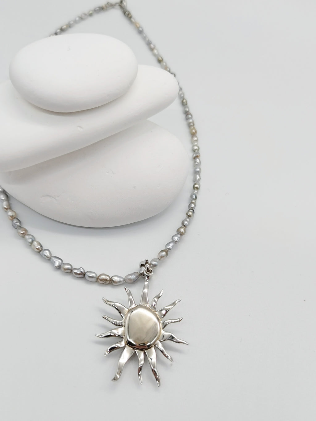 Details of the close back mounting of the white baroque pearl pendant, paired with a Tahitian keshi pearl necklace, lay flat on white background. 