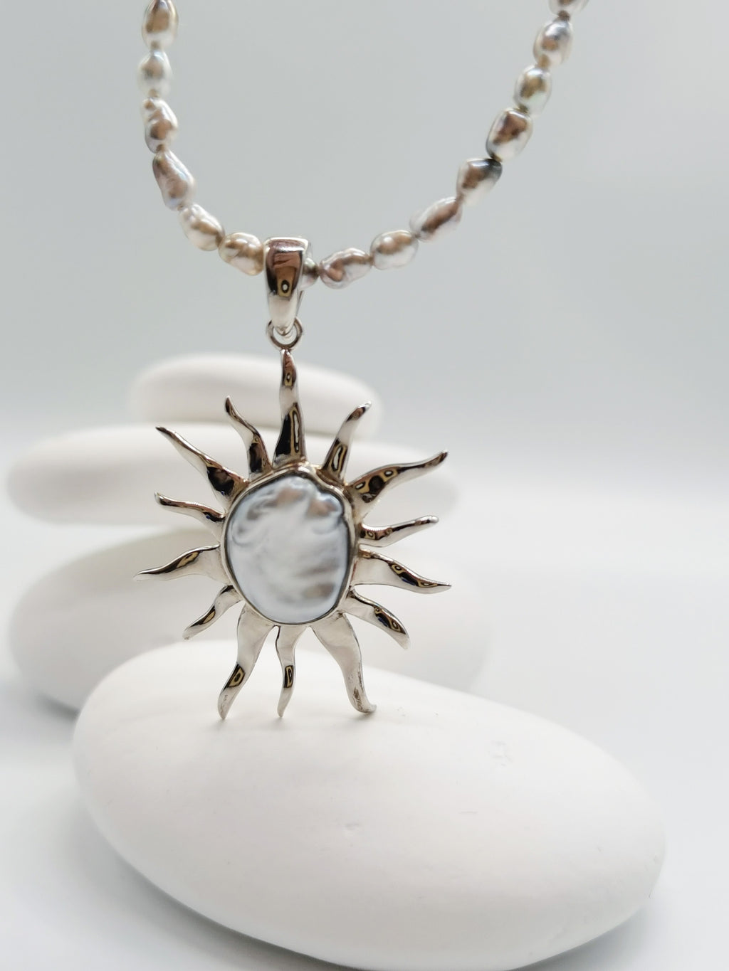 CLOSE UP VIEW OF BAROQUE SUNBURST PENDANT ON PAIRING NECKLACE suspended in the air