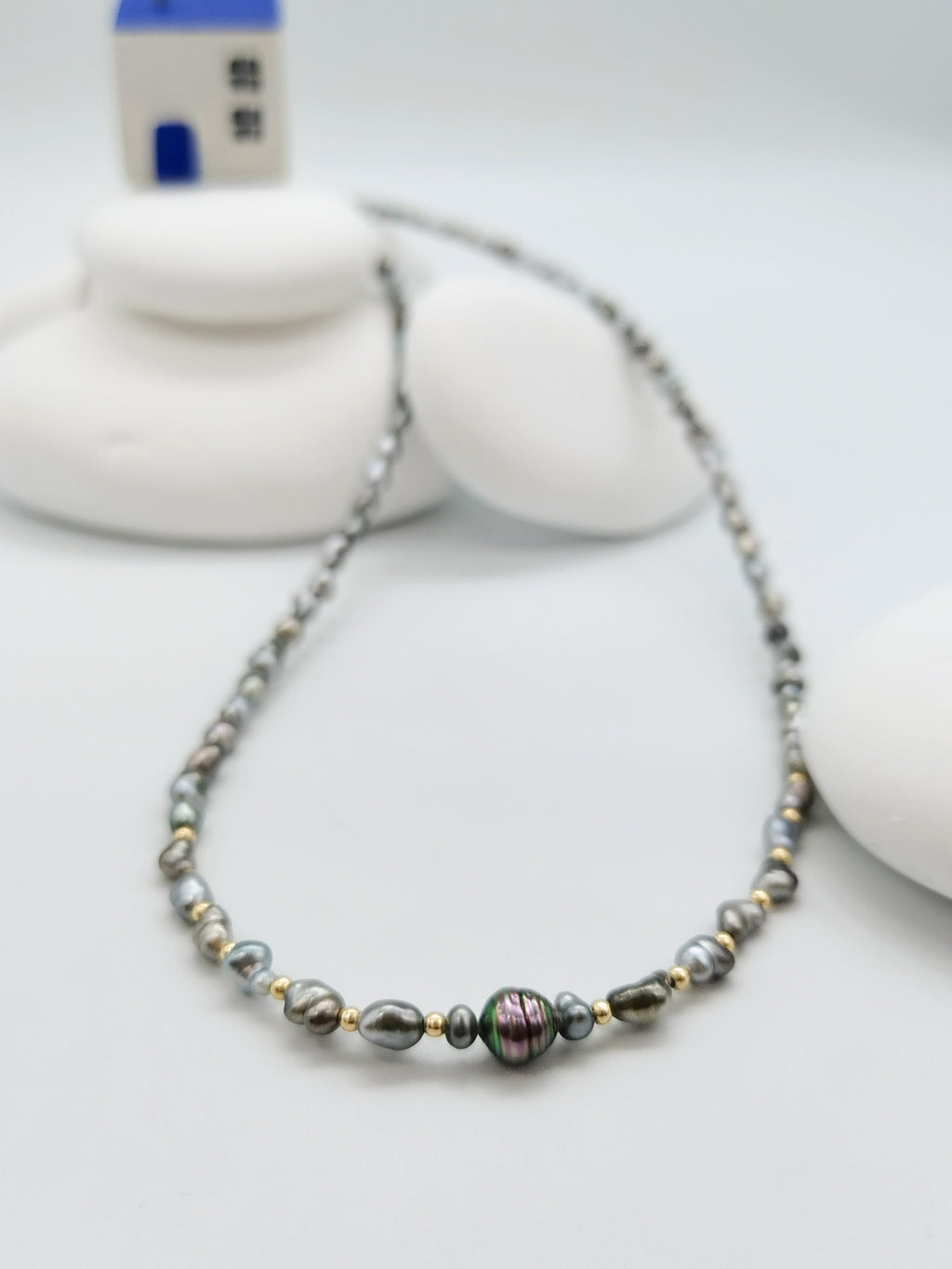 CLOSEUP DETAIL OF CENTRE PEARL OF HEART PEARL NECKLACE WITH GOLD BEADS, highlighting the special colour of the hero pearl. Strong contrast to the white stones soft-focused in the background
