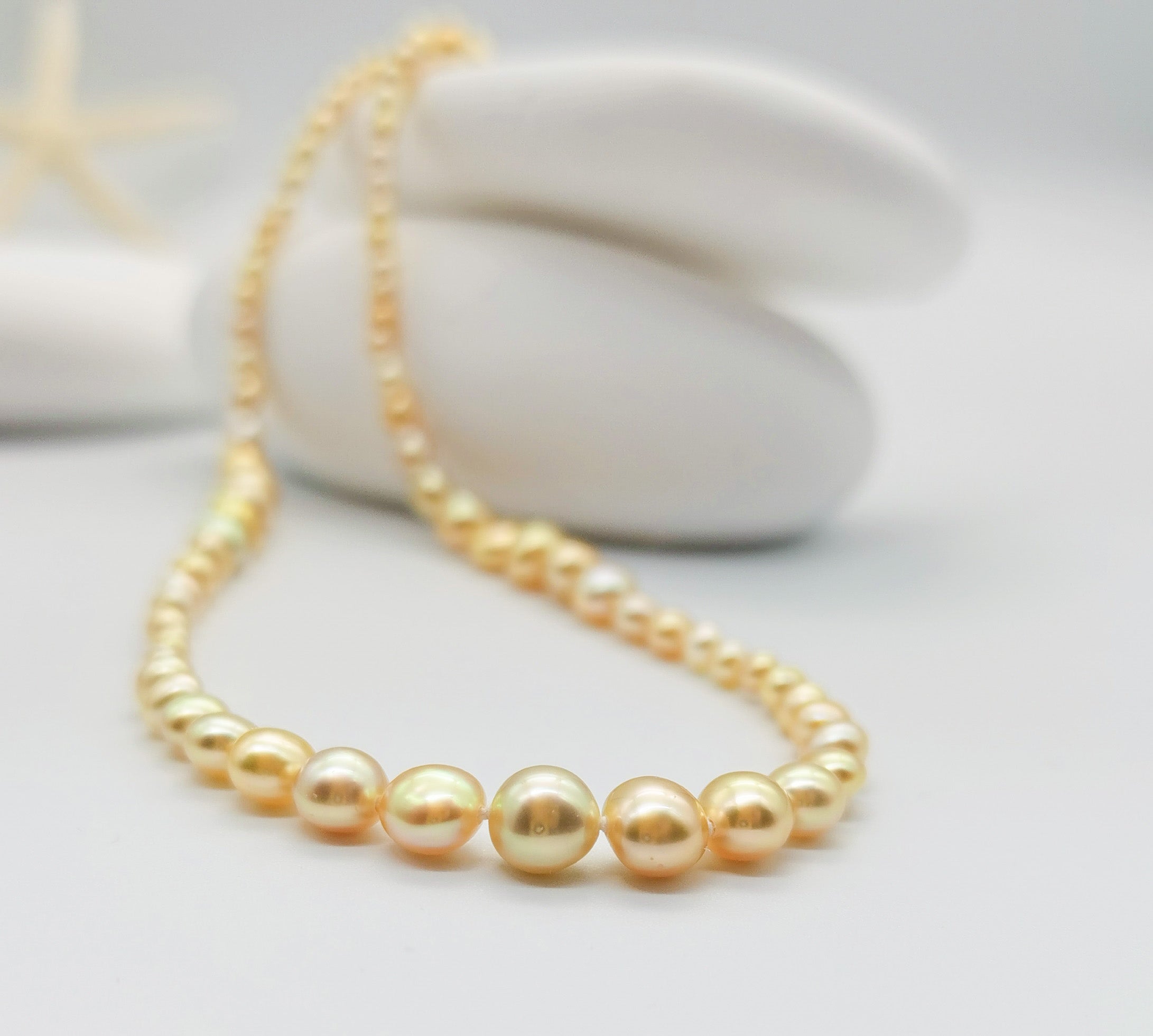 Close-up view of golden pearl necklace showing the lustrous graduated pearls and silver clasp against white stone backdrop