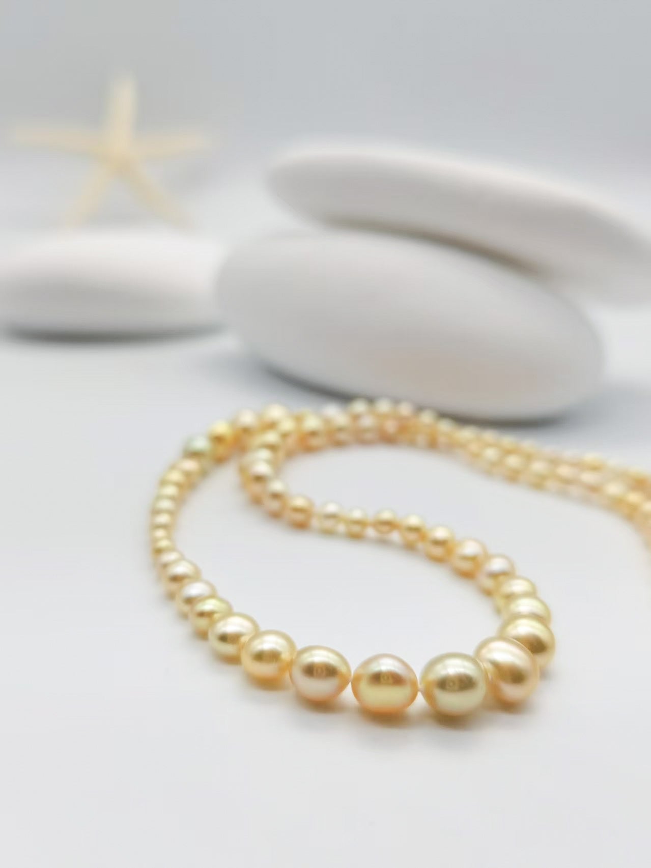 Detailed shot of golden pearl necklace highlighting the varying sizes of lustrous pearls from small to large in warm golden tones