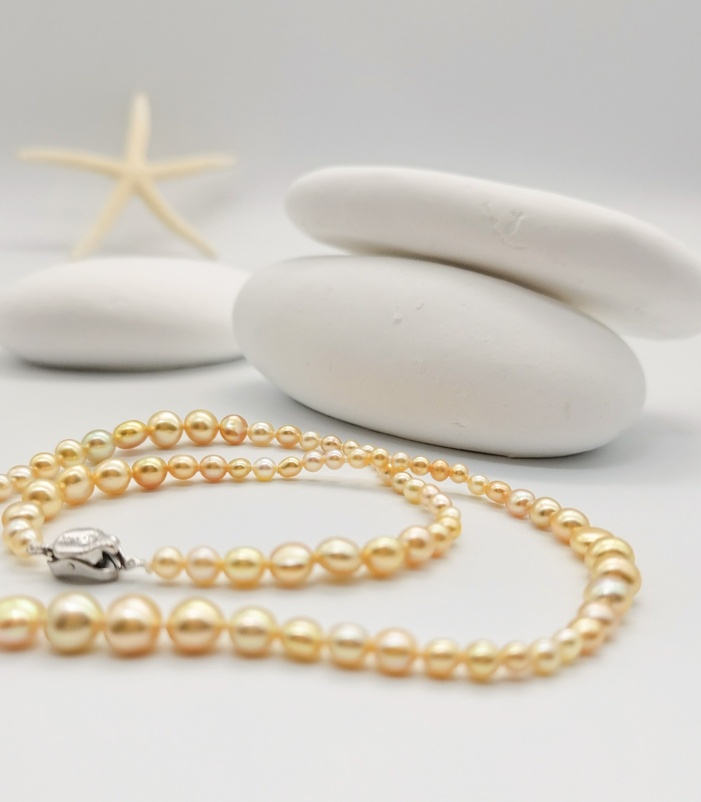 Golden pearl strand necklace with graduated pearls displayed on white stones with a starfish in a minimalist spa-like setting