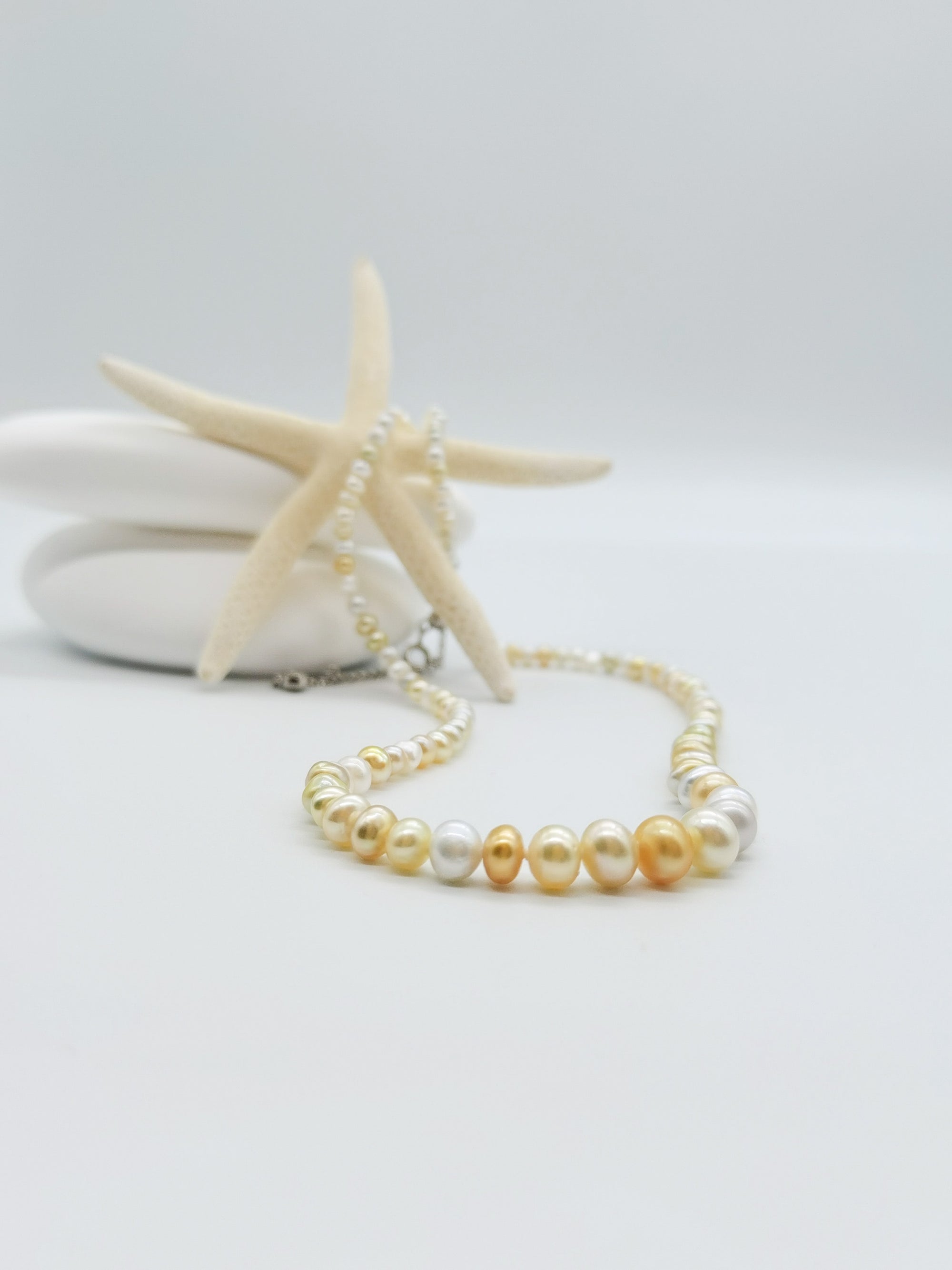 Close-up detail of white and cream pearl necklace draped over starfish against white stones, highlighting the lustrous graduated pearls and silver clasp