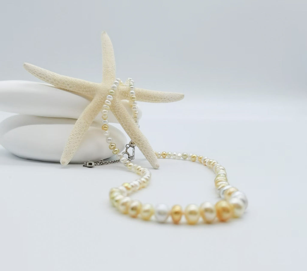White and cream pearl strand necklace elegantly draped around starfish on white stones, showcasing the graduated pearl design with mixed white, cream and golden tones