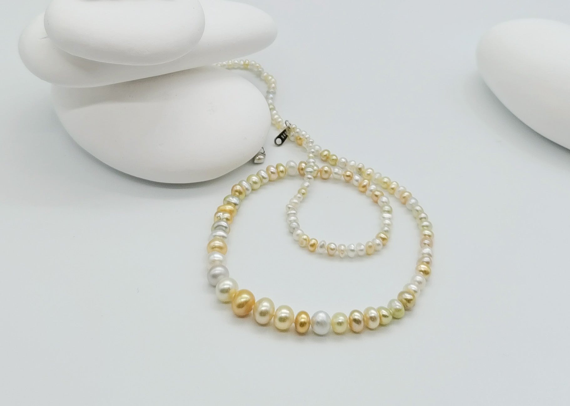 White and cream pearl strand necklace with graduated pearls displayed on white stones, showing the full length and silver clasp detail
