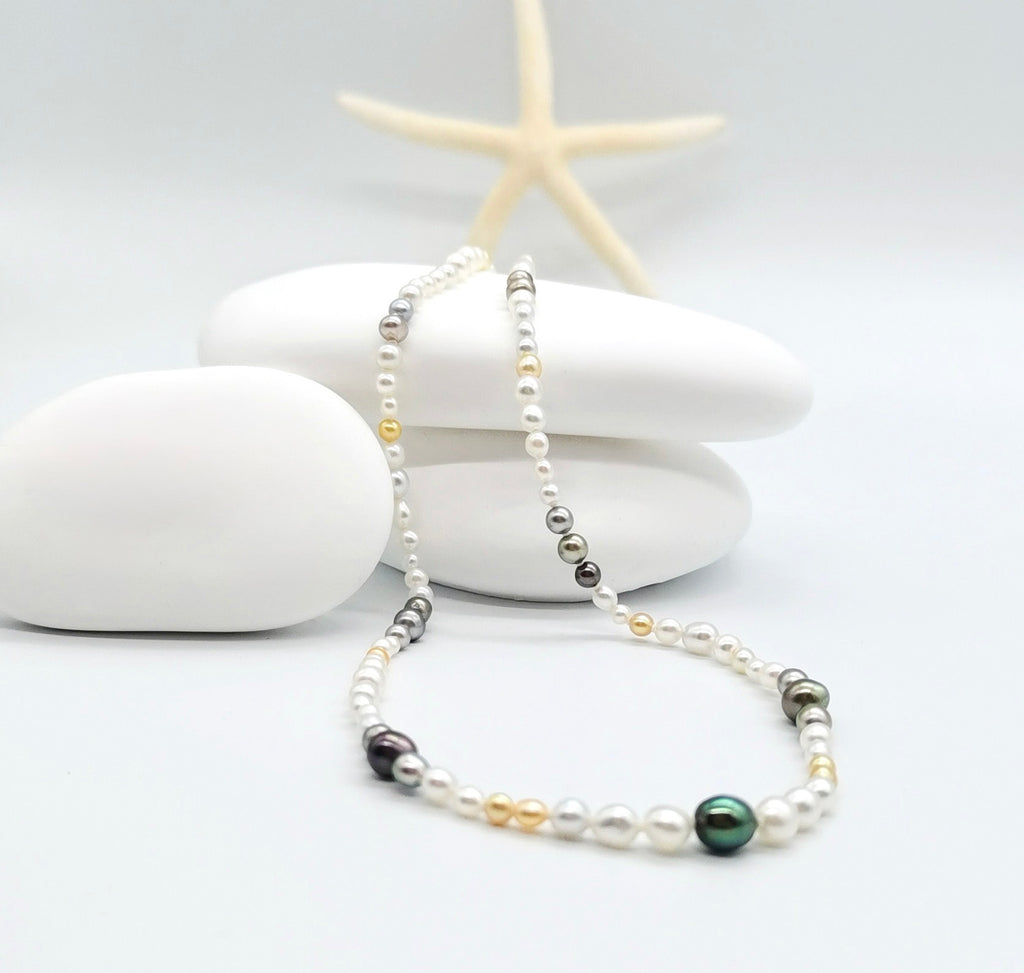 Multi-coloured pearl strand necklace elegantly draped in white shell with starfish accent, showcasing the beautiful mix of white, golden, silver, and dark green pearls in coastal styling