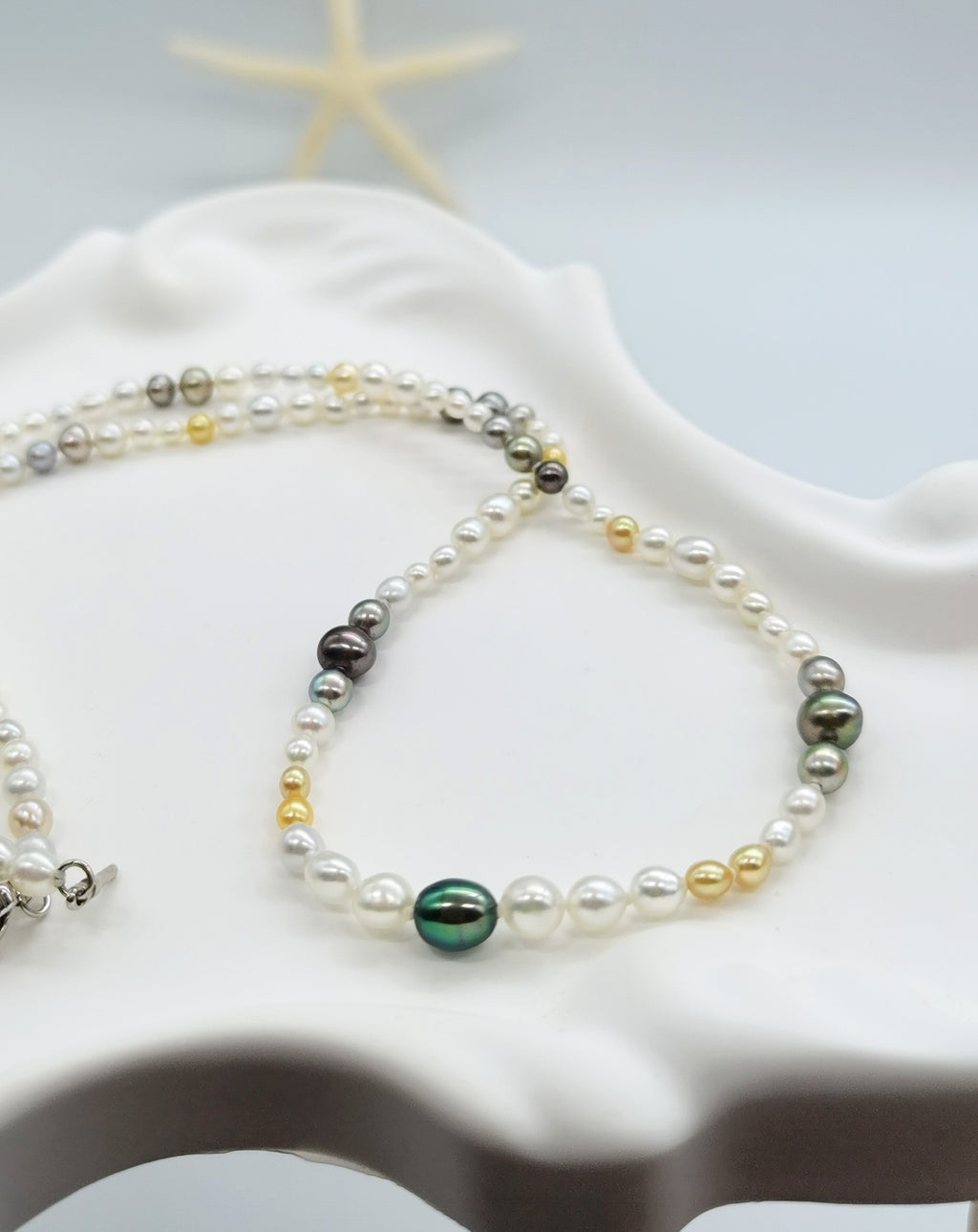 Close-up view of multi-coloured pearl necklace showcasing the variety of pearl colours including white, golden, silver, and dark green tones draped over white stones