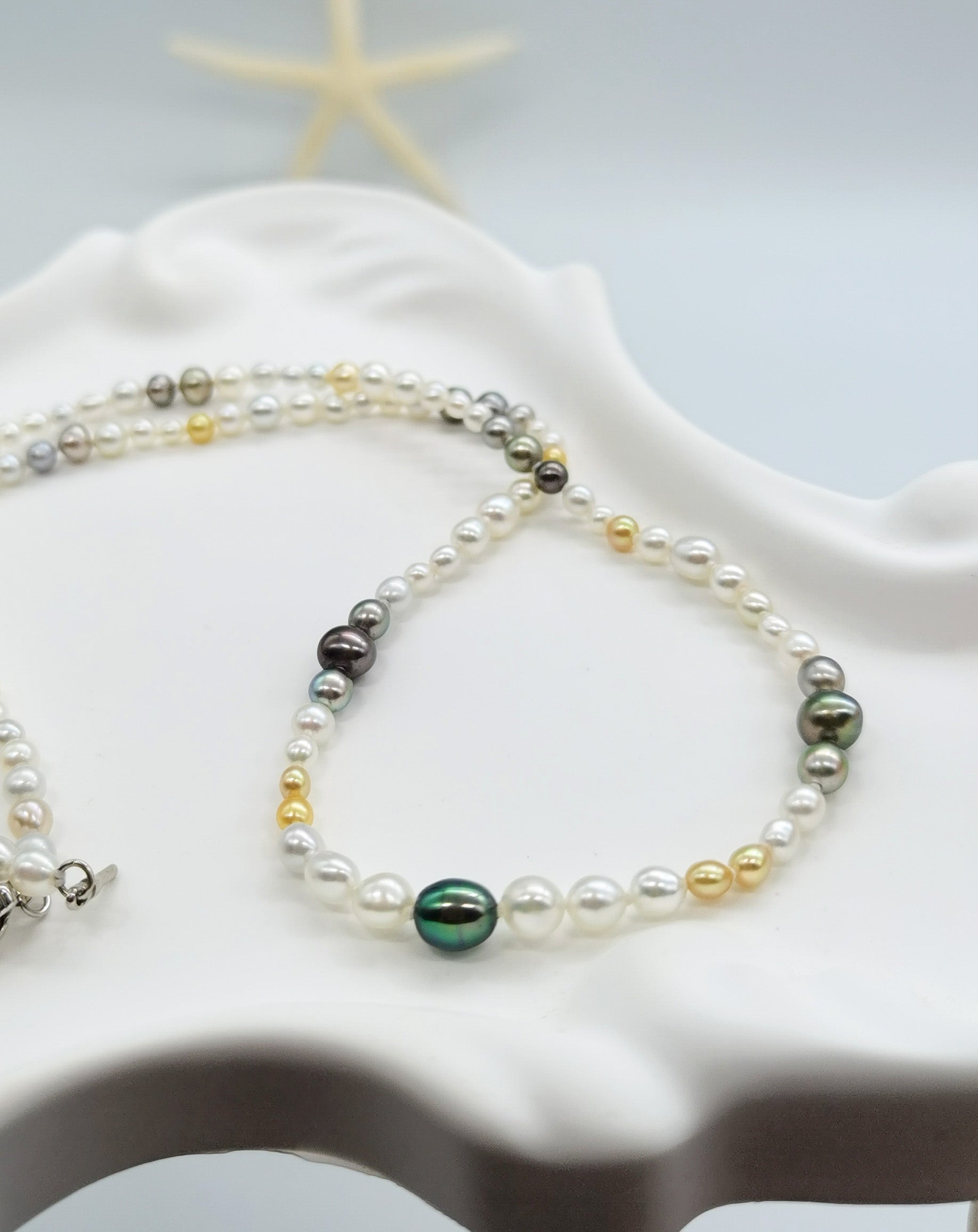 Close-up view of multi-coloured pearl necklace showcasing the variety of pearl colours including white, golden, silver, and dark green tones draped over white stones