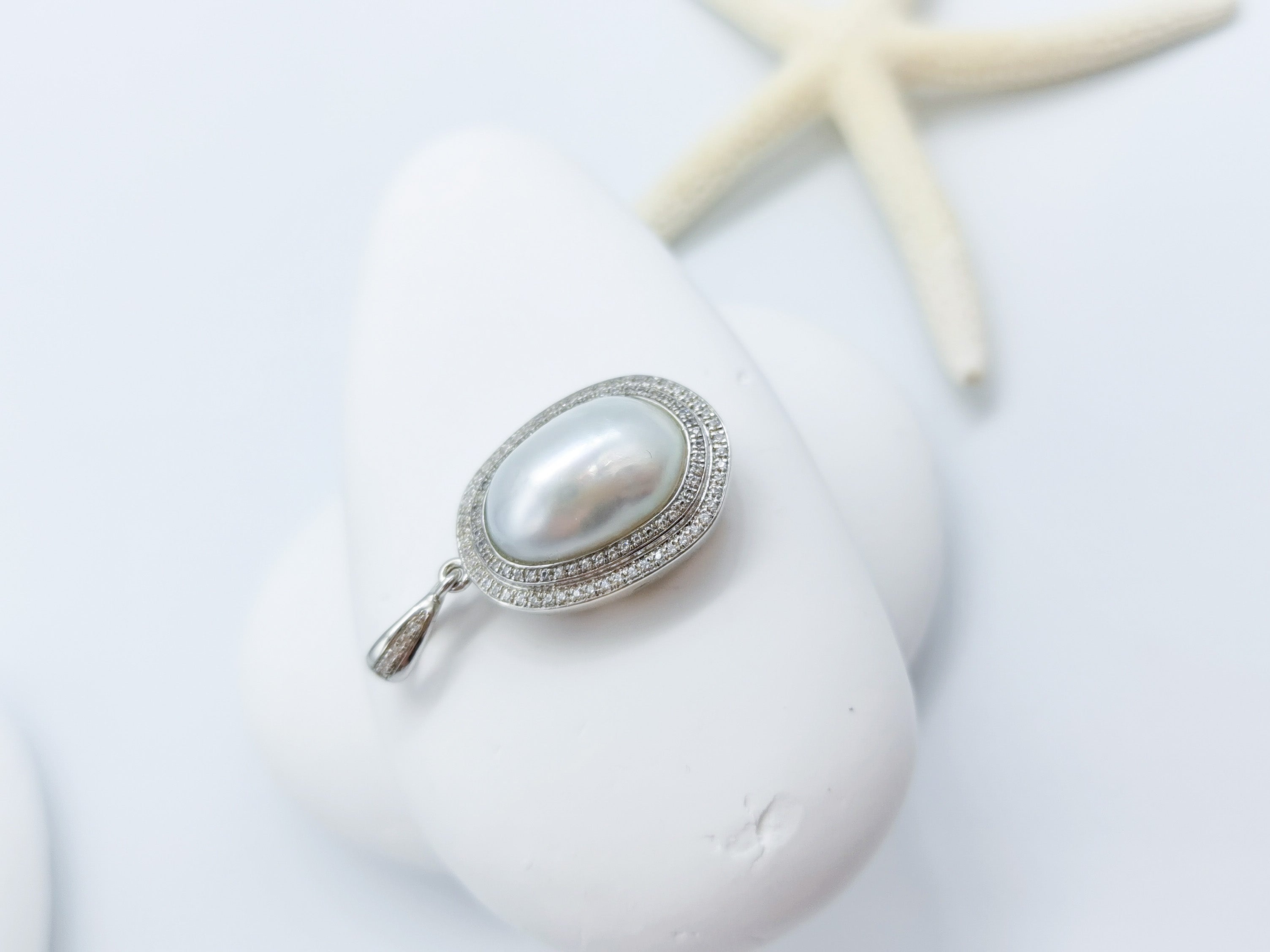 Close-up of grey baroque pearl necklace with lustrous white oval pearl and crystal halo pendant, displayed with starfish on clean white background