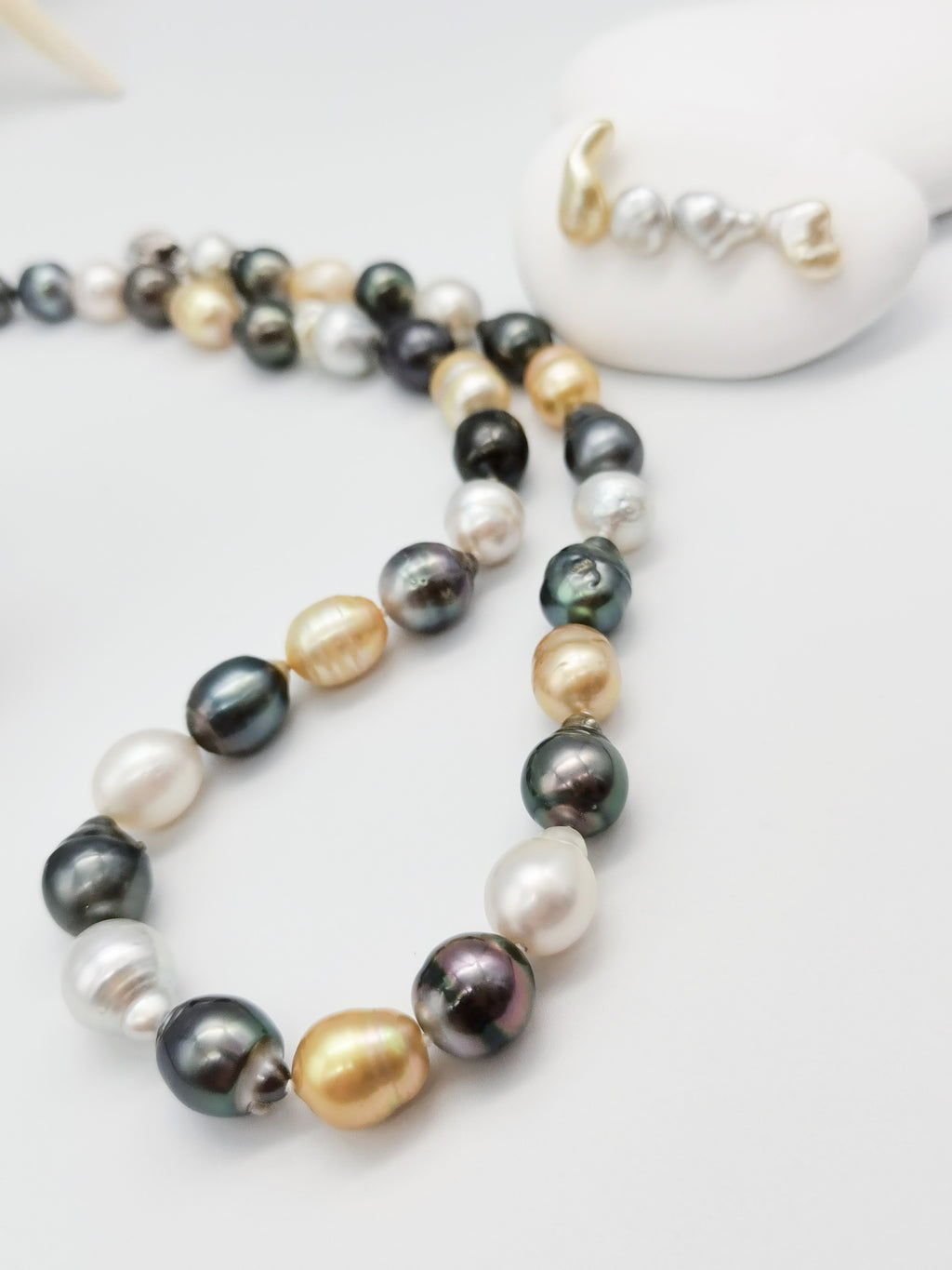 Multicoloured baroque pearl necklace gracefully displayed on white stones with starfish backdrop, showcasing the full length and natural lustre of the varied pearl colours
