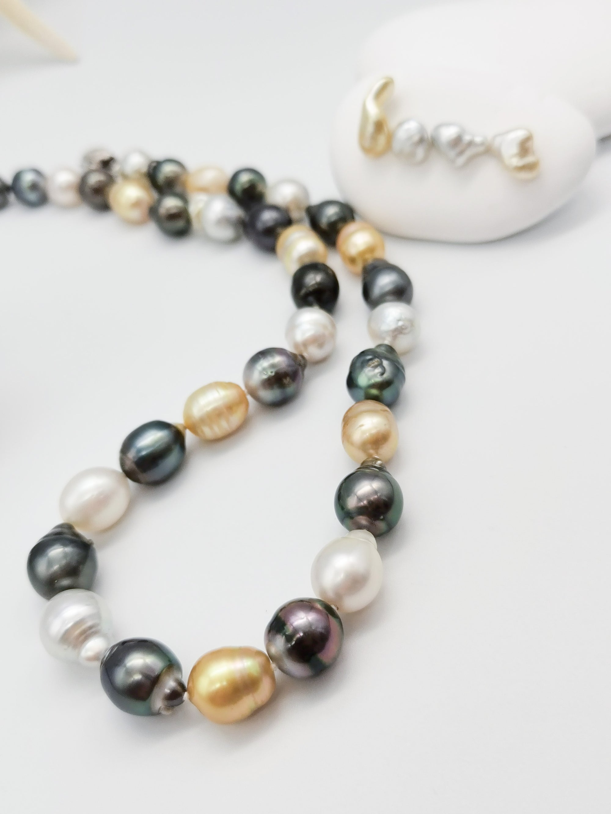Multicoloured baroque pearl necklace gracefully displayed on white stones with starfish backdrop, showcasing the full length and natural lustre of the varied pearl colours