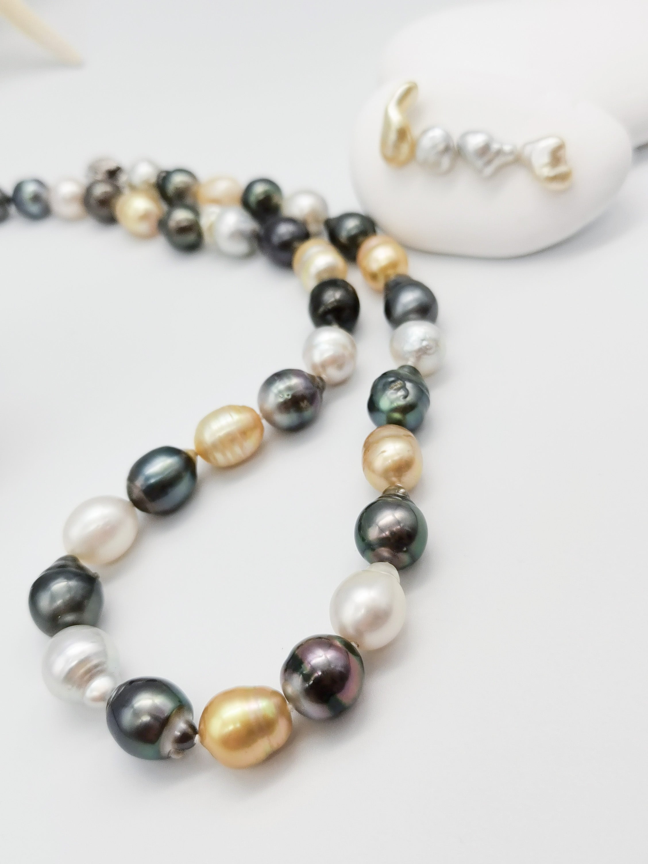 Multicoloured baroque pearl necklace gracefully displayed on white stones with starfish backdrop, showcasing the full length and natural lustre of the varied pearl colours