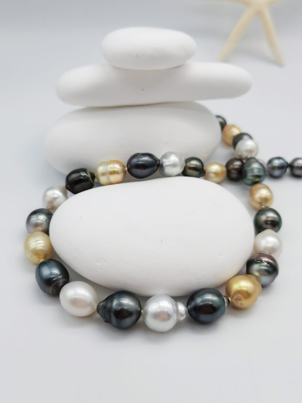 Multicoloured baroque pearl necklace elegantly draped around smooth white stones with starfish accent, highlighting the beautiful mix of pearl colours and organic shapes