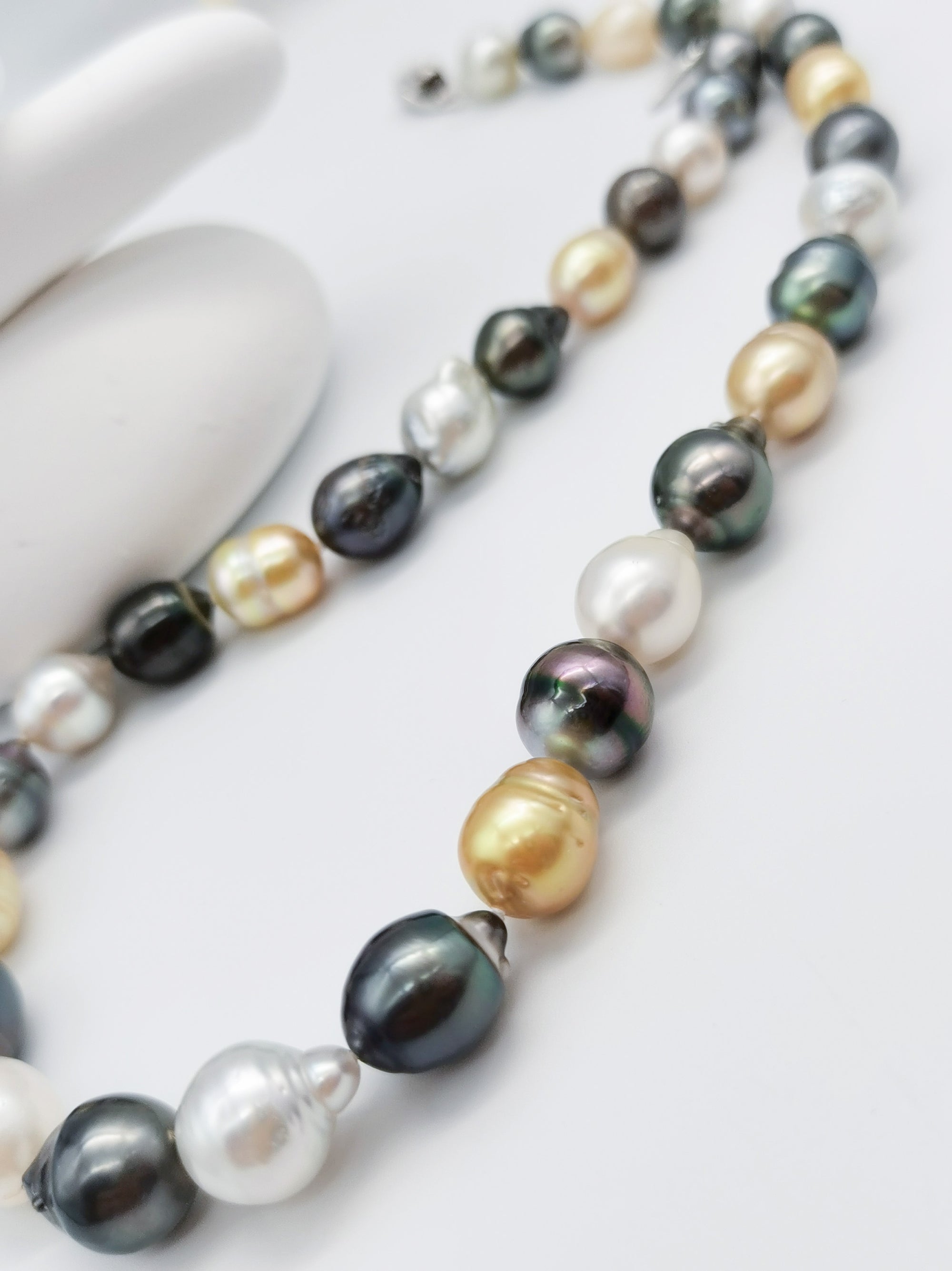 Close-up detail of multicoloured baroque pearl strand showcasing the lustrous variety of white, golden, dark green and black pearls with natural baroque shapes