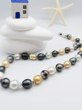 Multicoloured baroque pearl strand necklace artistically arranged with decorative blue house ornament and starfish on stacked white stones in coastal-themed styling