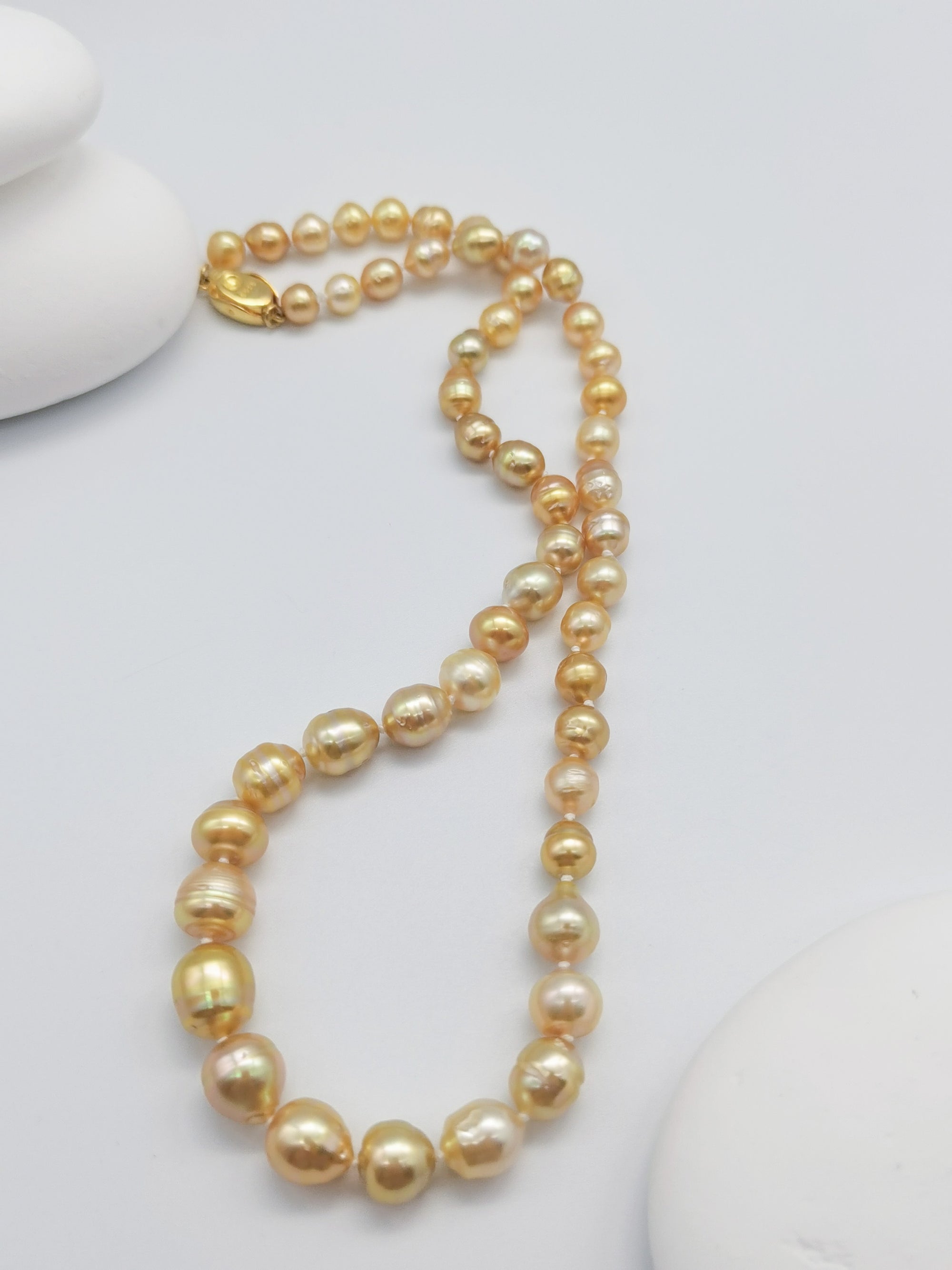 Golden baroque pearl strand necklace with gold clasp elegantly displayed on white stones with starfish accent, highlighting the natural baroque shapes and warm golden lustre