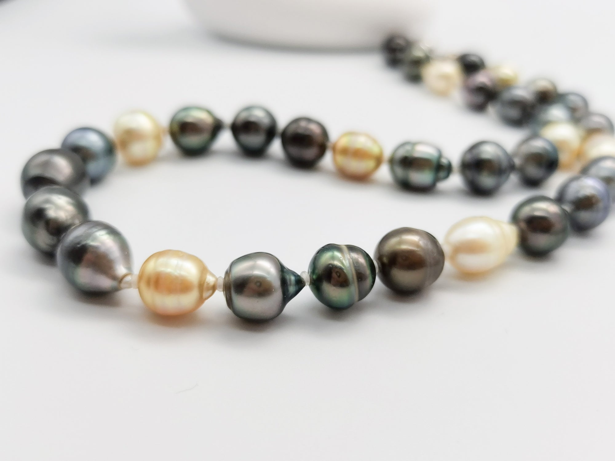 Detailed close-up of multicoloured baroque pearl necklace showcasing the lustrous dark green, black, golden and white pearls with natural baroque shapes on clean white background