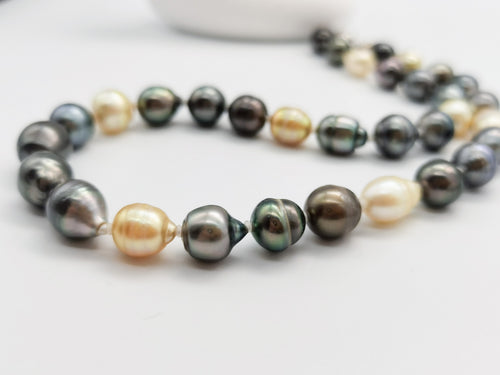 Detailed close-up of multicoloured baroque pearl necklace showcasing the lustrous dark green, black, golden and white pearls with natural baroque shapes on clean white background