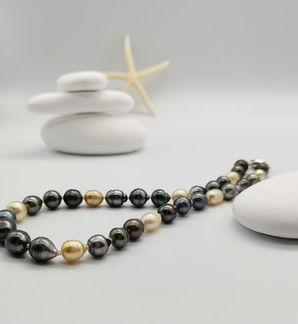Full-length view of multicoloured baroque pearl necklace with silver clasp gracefully arranged in front of white stones, showcasing the complete design with varied pearl colours and shapes