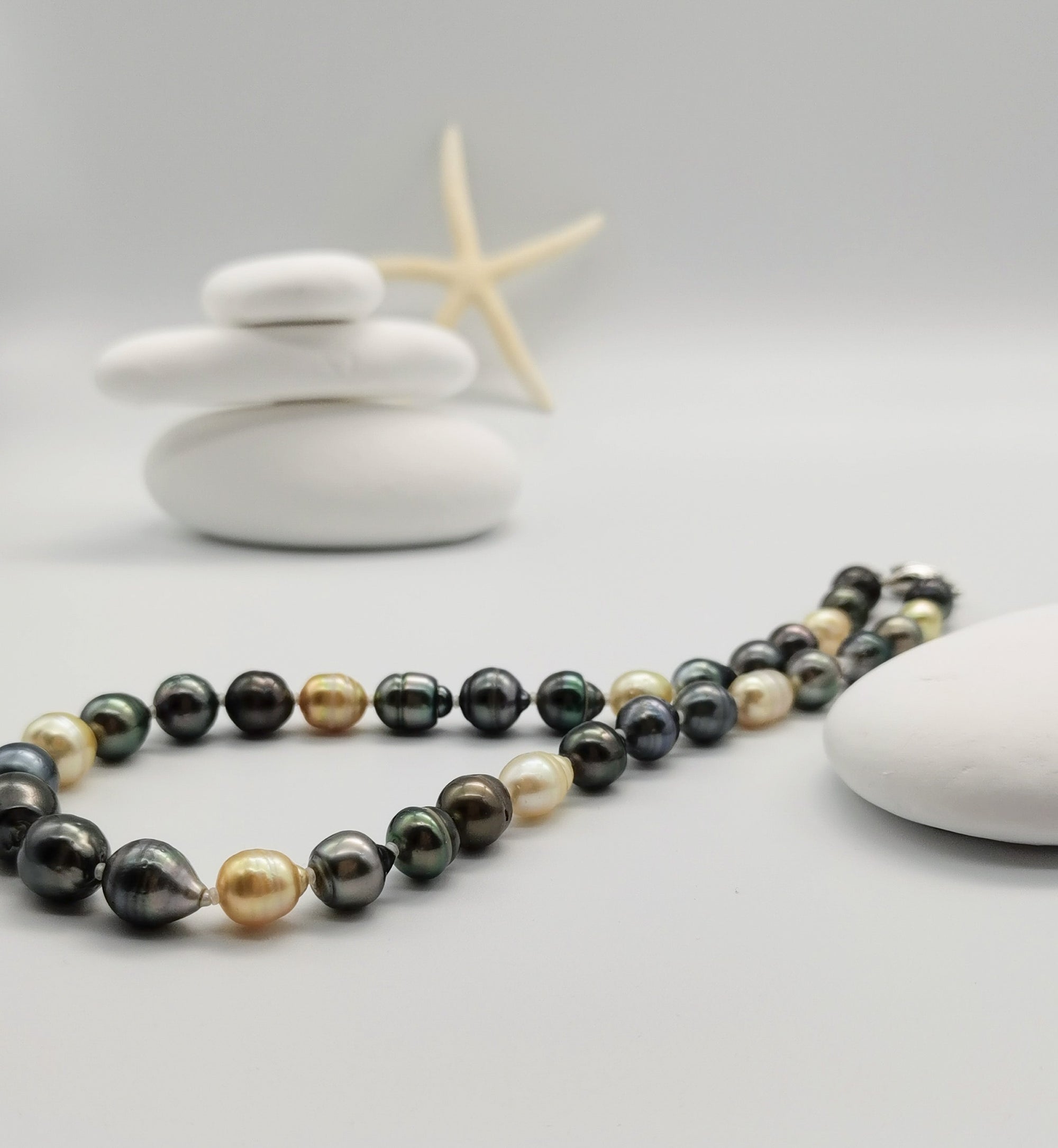 Full-length view of multicoloured baroque pearl necklace with silver clasp gracefully arranged in front of white stones, showcasing the complete design with varied pearl colours and shapes