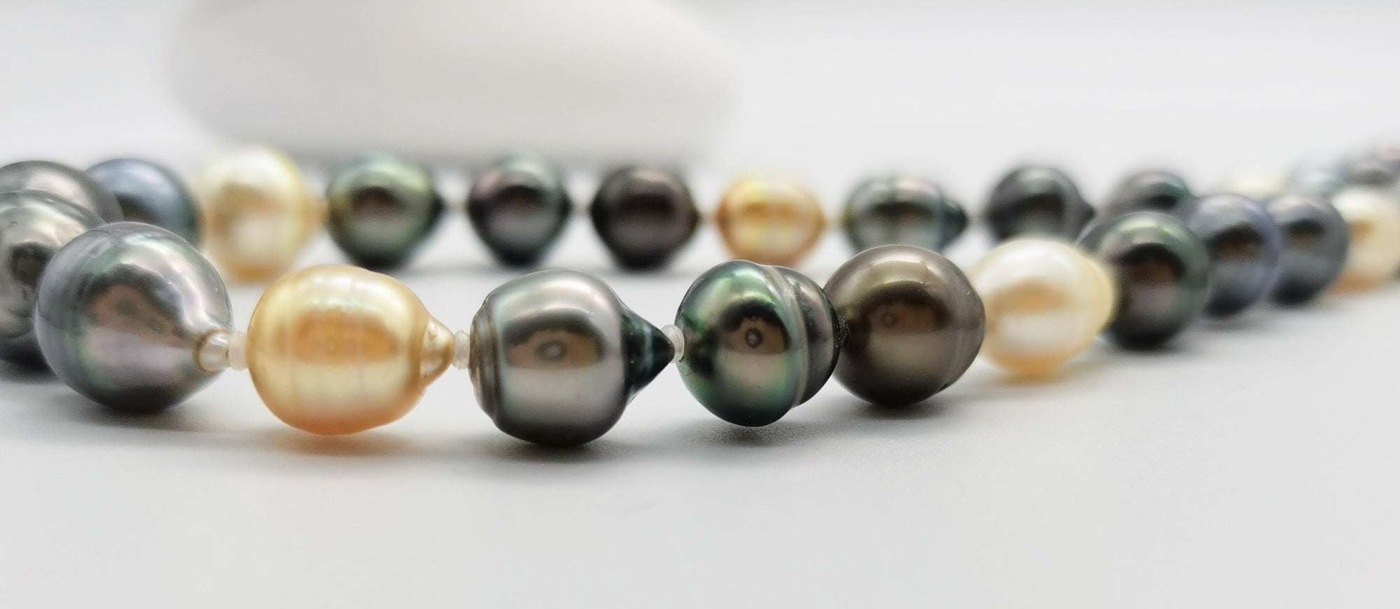 Close-up view of multicoloured baroque pearl necklace with dark green, black, golden and white pearls, highlighting the natural baroque shapes and lustrous finish