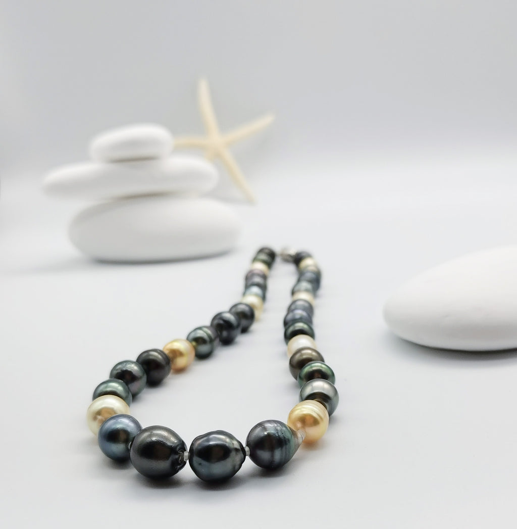 Multicoloured baroque pearl strand necklace artistically arranged in front of stacked white stones with starfish backdrop, displaying the beautiful mix of dark and golden pearl tones