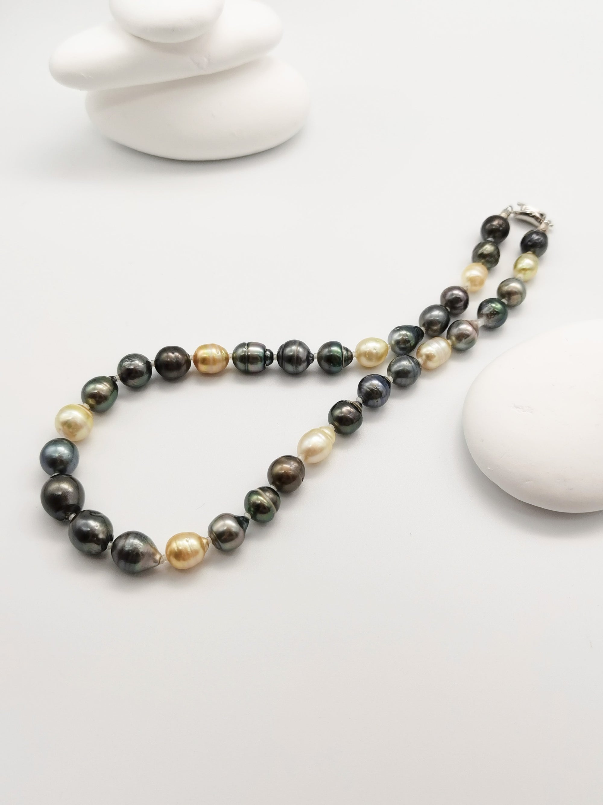Multicoloured baroque pearl necklace elegantly displayed on stacked white stones with starfish backdrop in zen-like composition, highlighting the full strand length