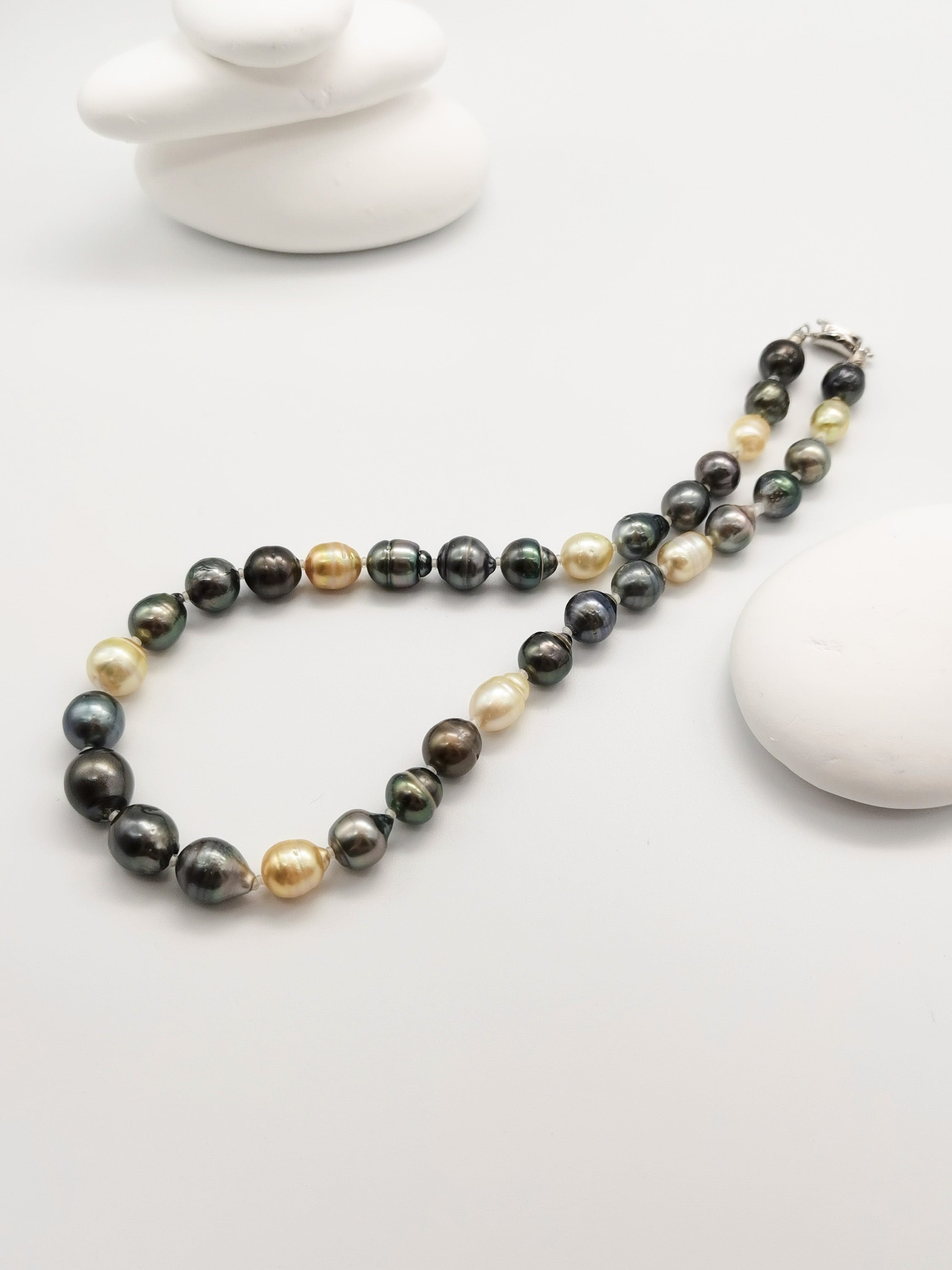 Multicoloured baroque pearl necklace elegantly displayed on stacked white stones with starfish backdrop in zen-like composition, highlighting the full strand length