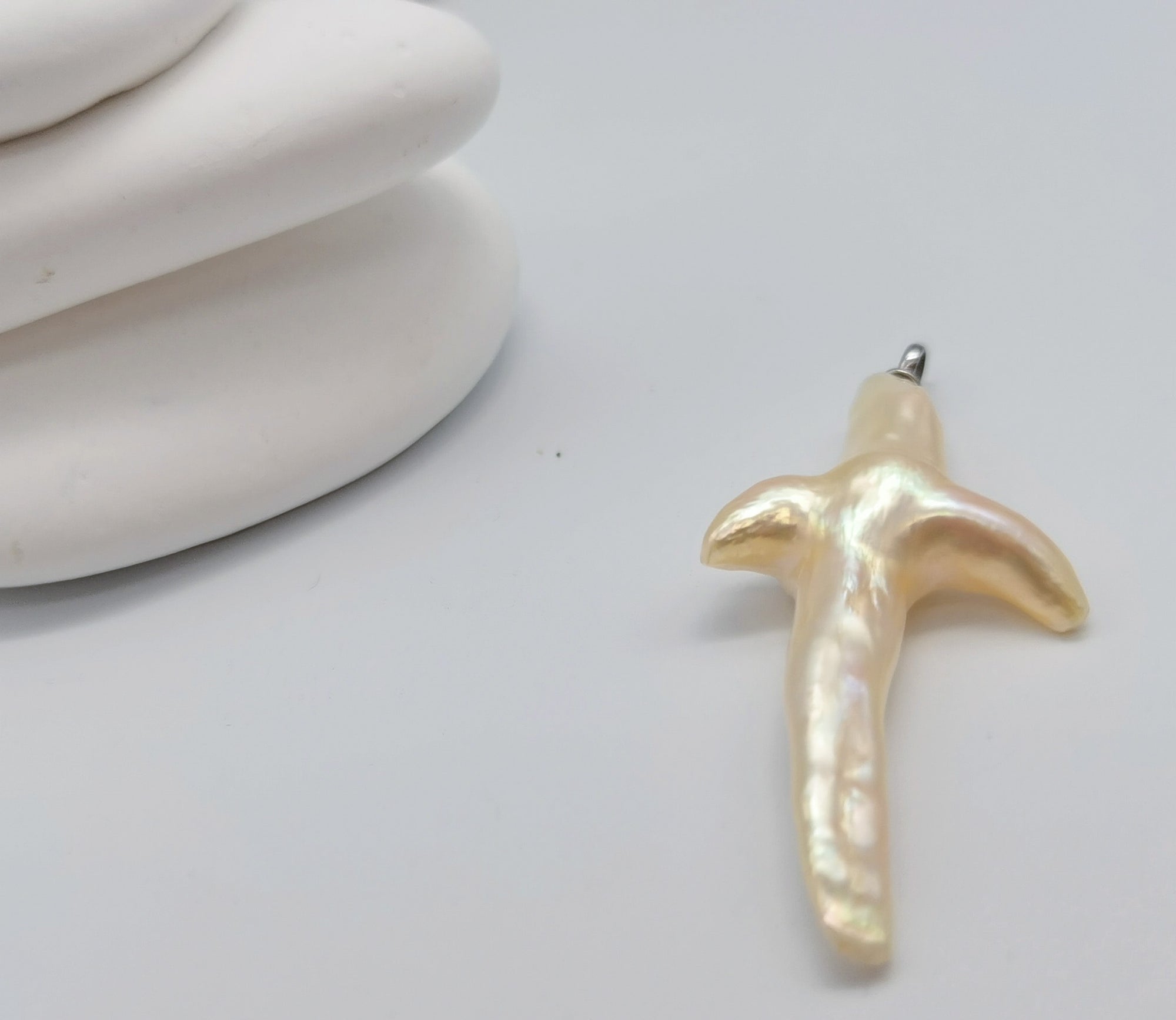 Cross-shaped baroque pearl pendant showing natural cross form nucleus-free freshwater pearl sterling silver bail white styling