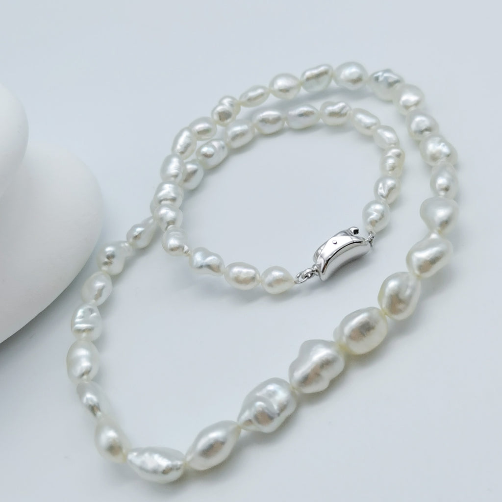 South Sea white keshi pearl strand necklace displayed in full length showing silver clasp and graduated baroque pearls on white stones background