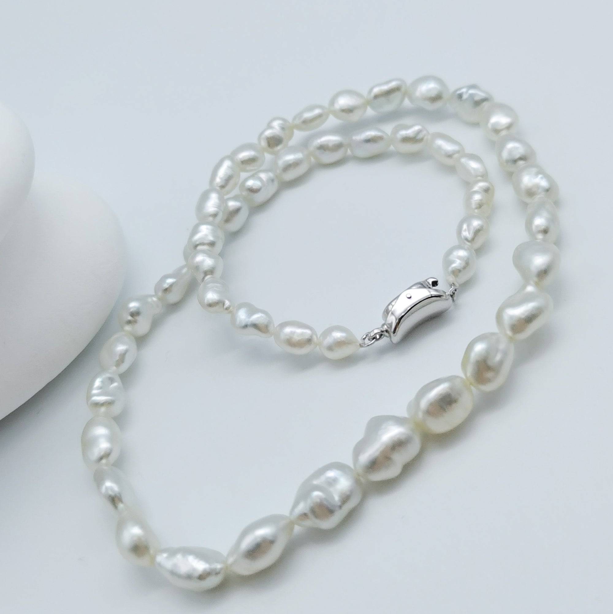 South Sea white keshi pearl strand necklace displayed in full length showing silver clasp and graduated baroque pearls on white stones background