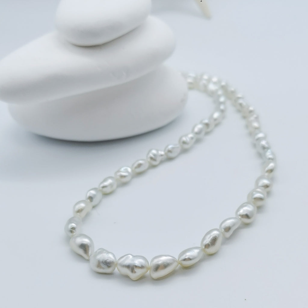 South Sea white keshi pearl strand necklace artistically arranged with white stones background showcasing natural irregular pearl shapes