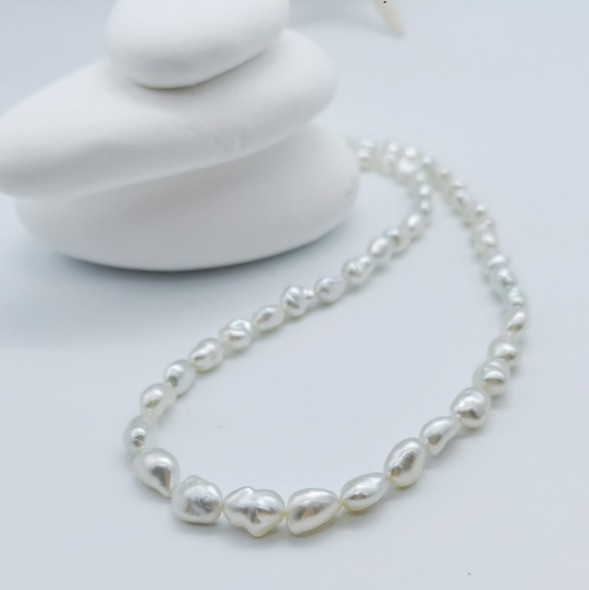 South Sea white keshi pearl strand necklace artistically arranged with white stones background showcasing natural irregular pearl shapes
