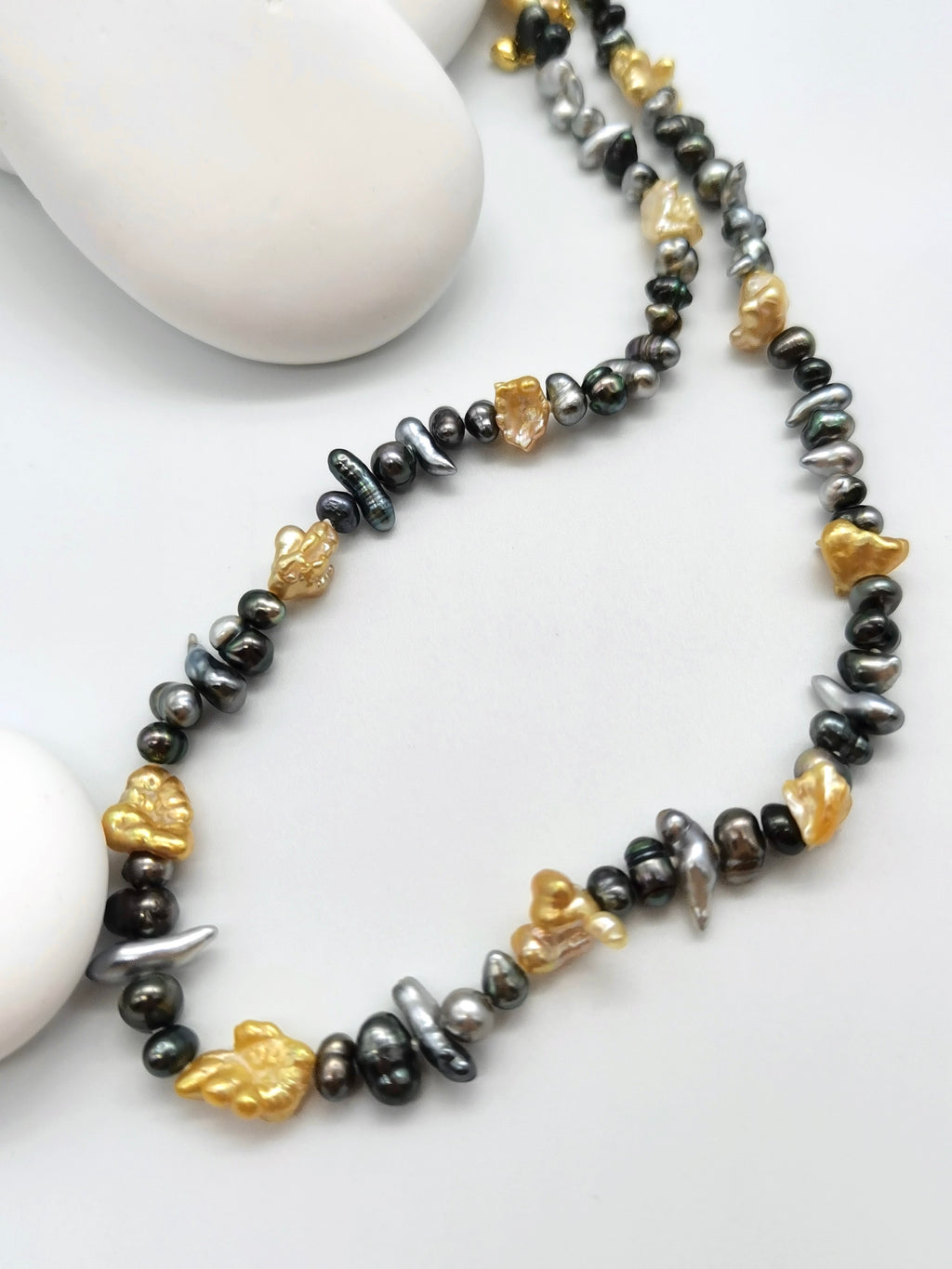 Close-up detail of mixed colour Tahitian keshi pearls with silver and black body tones alongside rugged gold South Sea keshi pearls