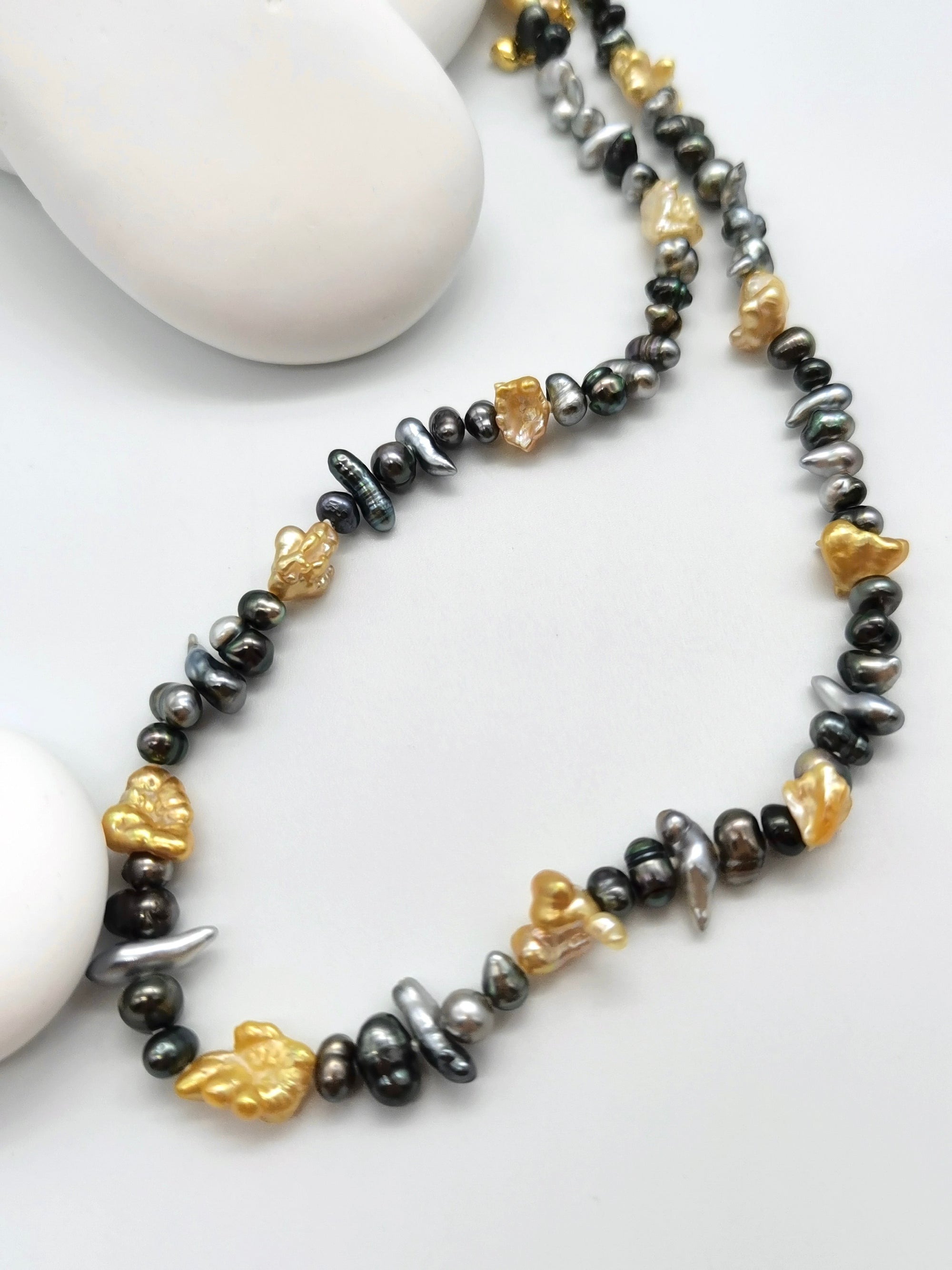 Close-up detail of mixed colour Tahitian keshi pearls with silver and black body tones alongside rugged gold South Sea keshi pearls