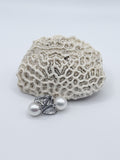 White freshwater pearl earrings with detailed silver teardrop frames showcasing decorative metalwork, artistically positioned against textured coral backdrop