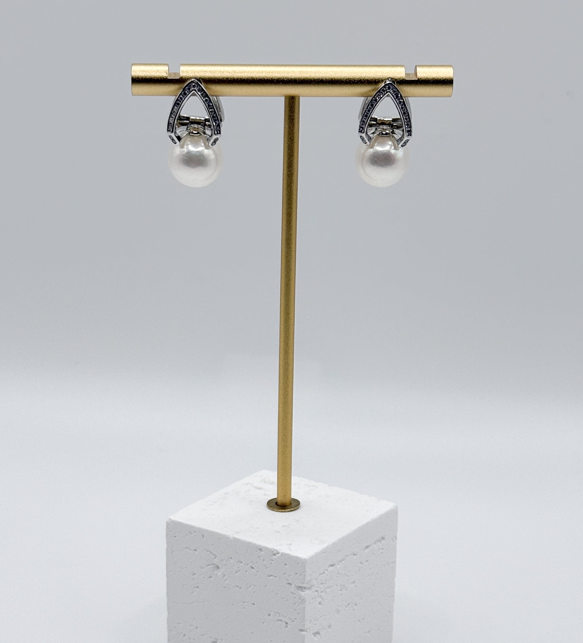White freshwater pearl earrings with ornate silver teardrop settings featuring intricate filigree design, displayed on gold earring stand
