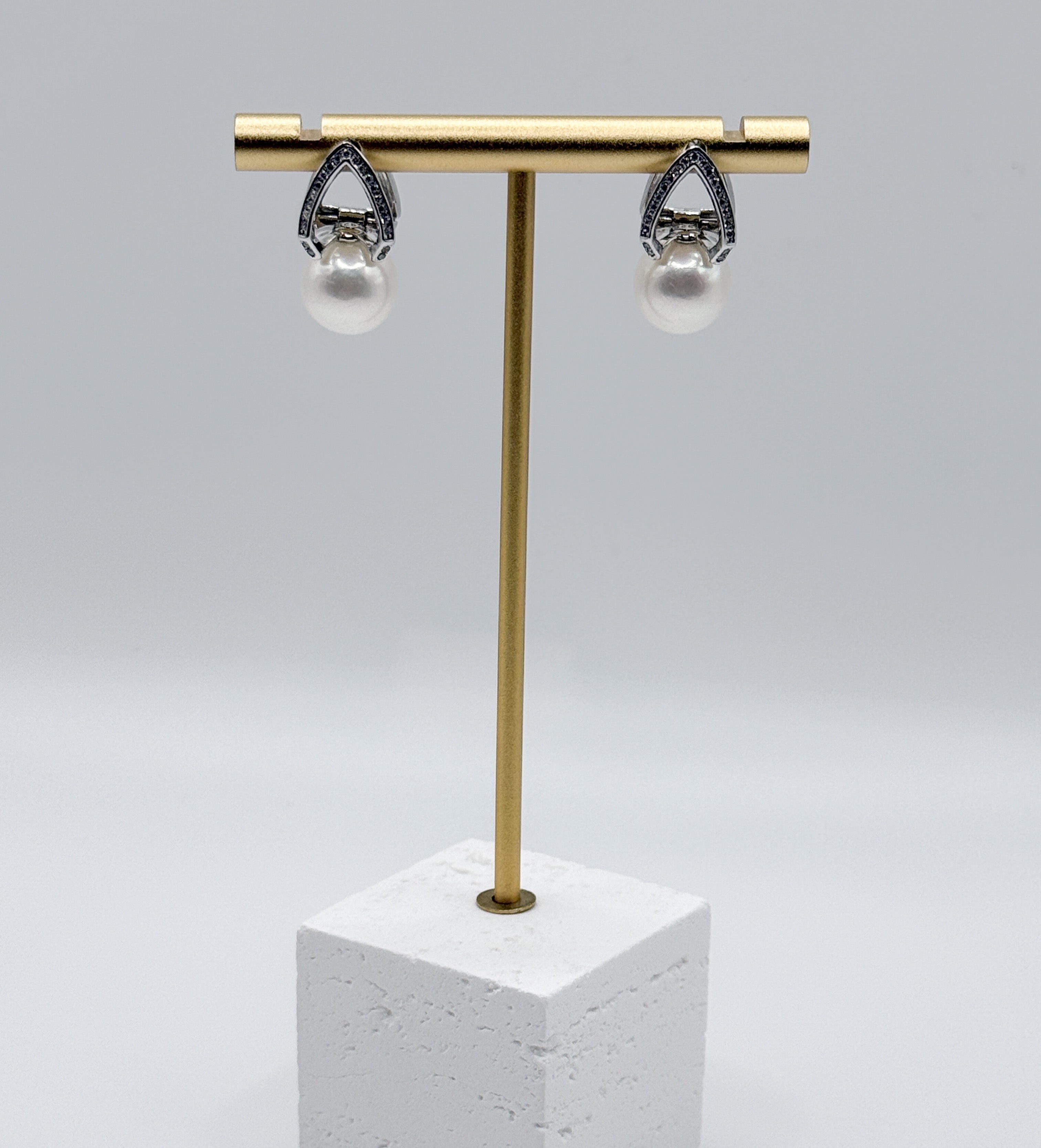 White freshwater pearl earrings with ornate silver teardrop settings featuring intricate filigree design, displayed on gold earring stand