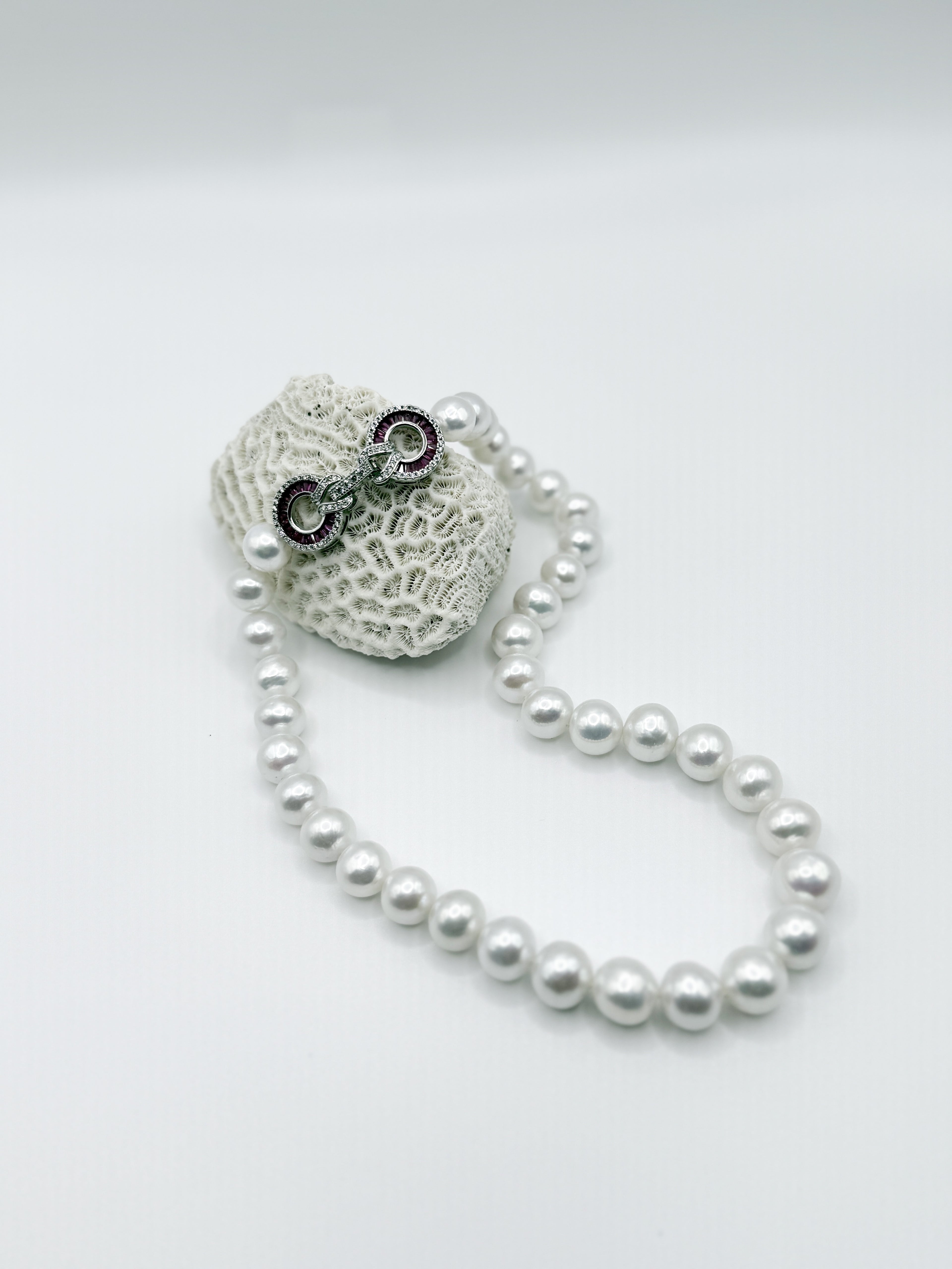 White freshwater pearl strand necklace with jewelled infinity clasp artistically positioned with white coral backdrop, highlighting the lustrous round pearls