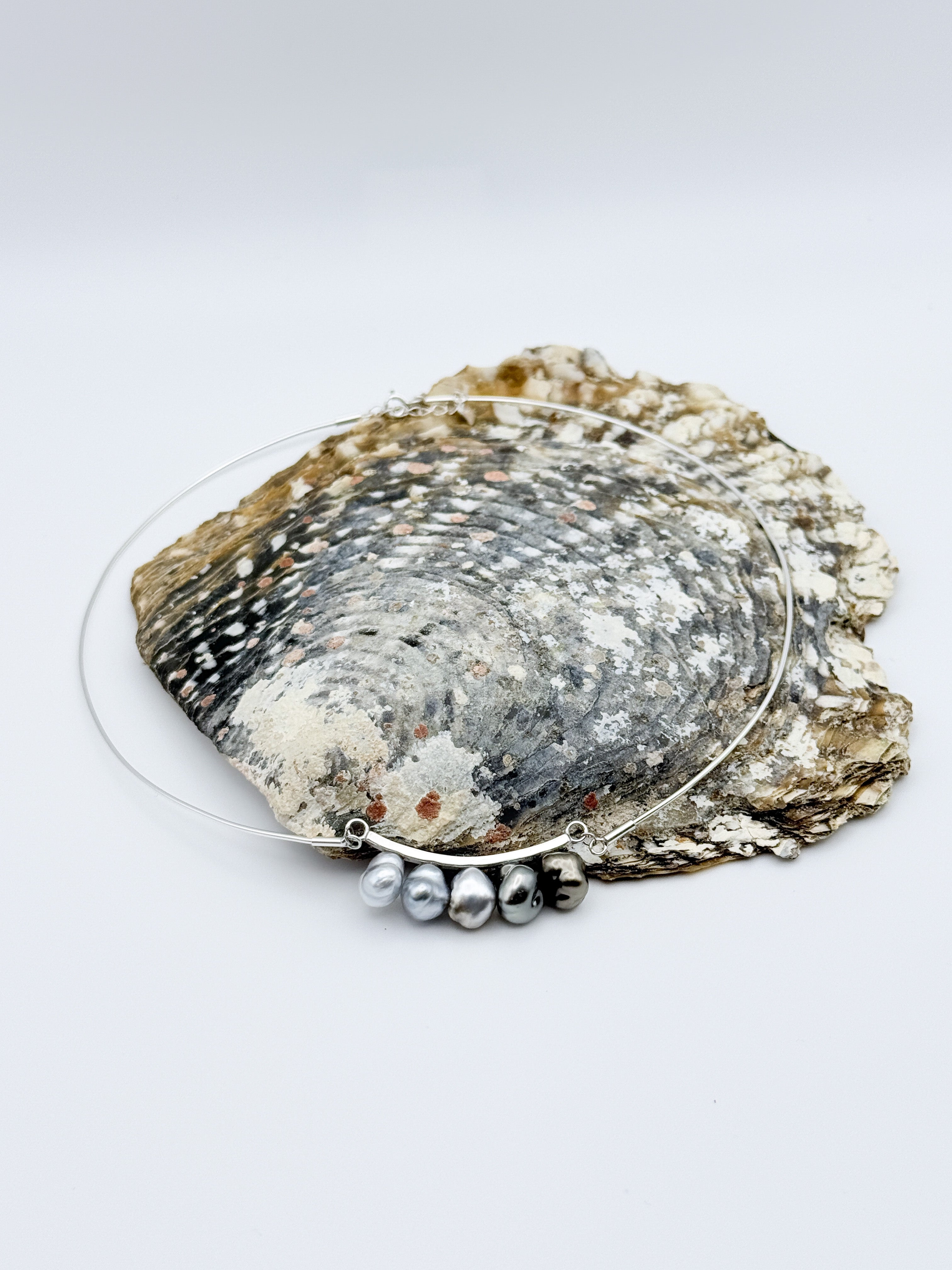 Side view highlighting curved silver bar and spacing between pearls