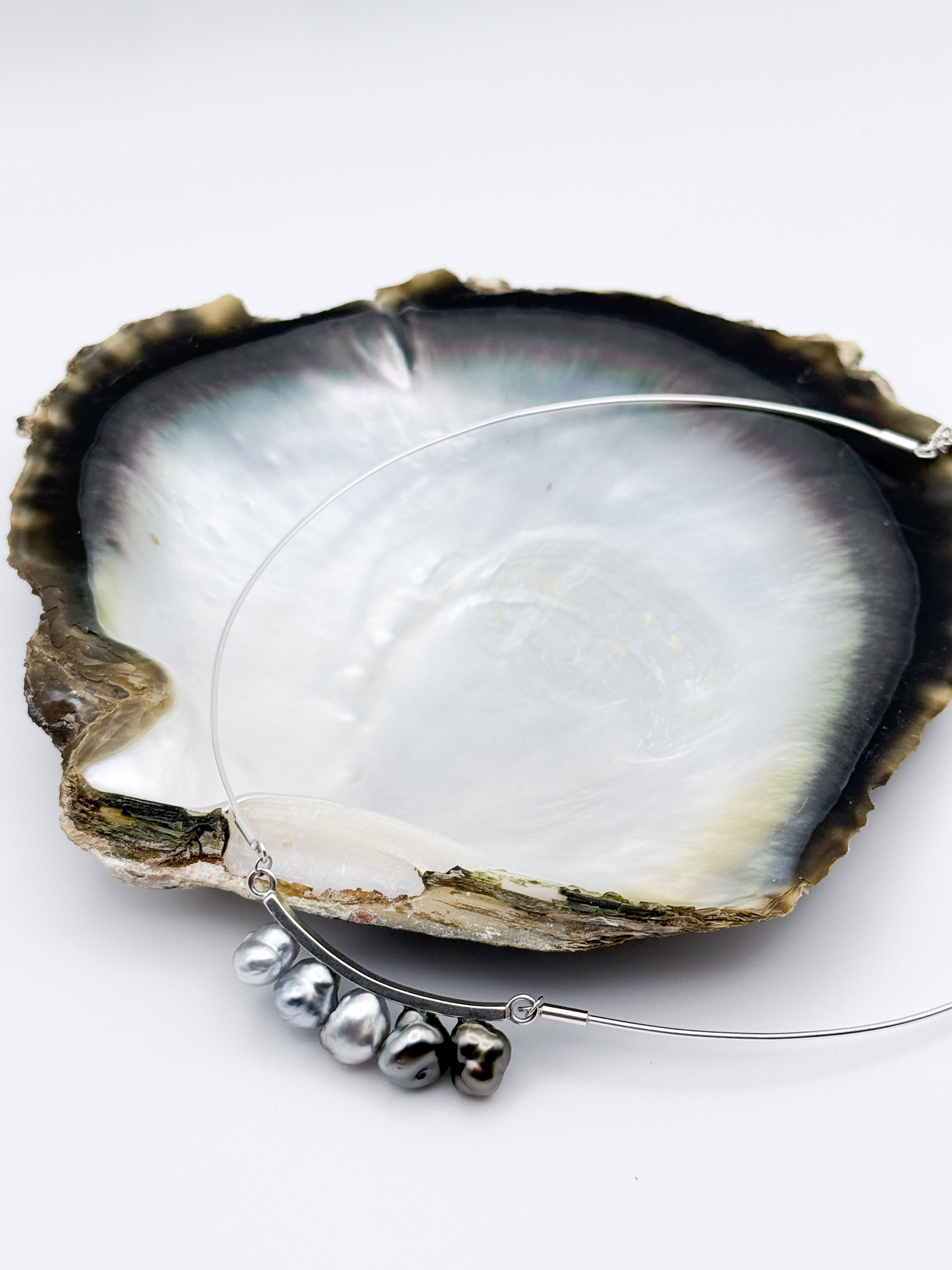 Tooth Fairy necklace with five Tahitian Keshi pearls on curved silver bar and neck wire against a black lipped oyster shell
