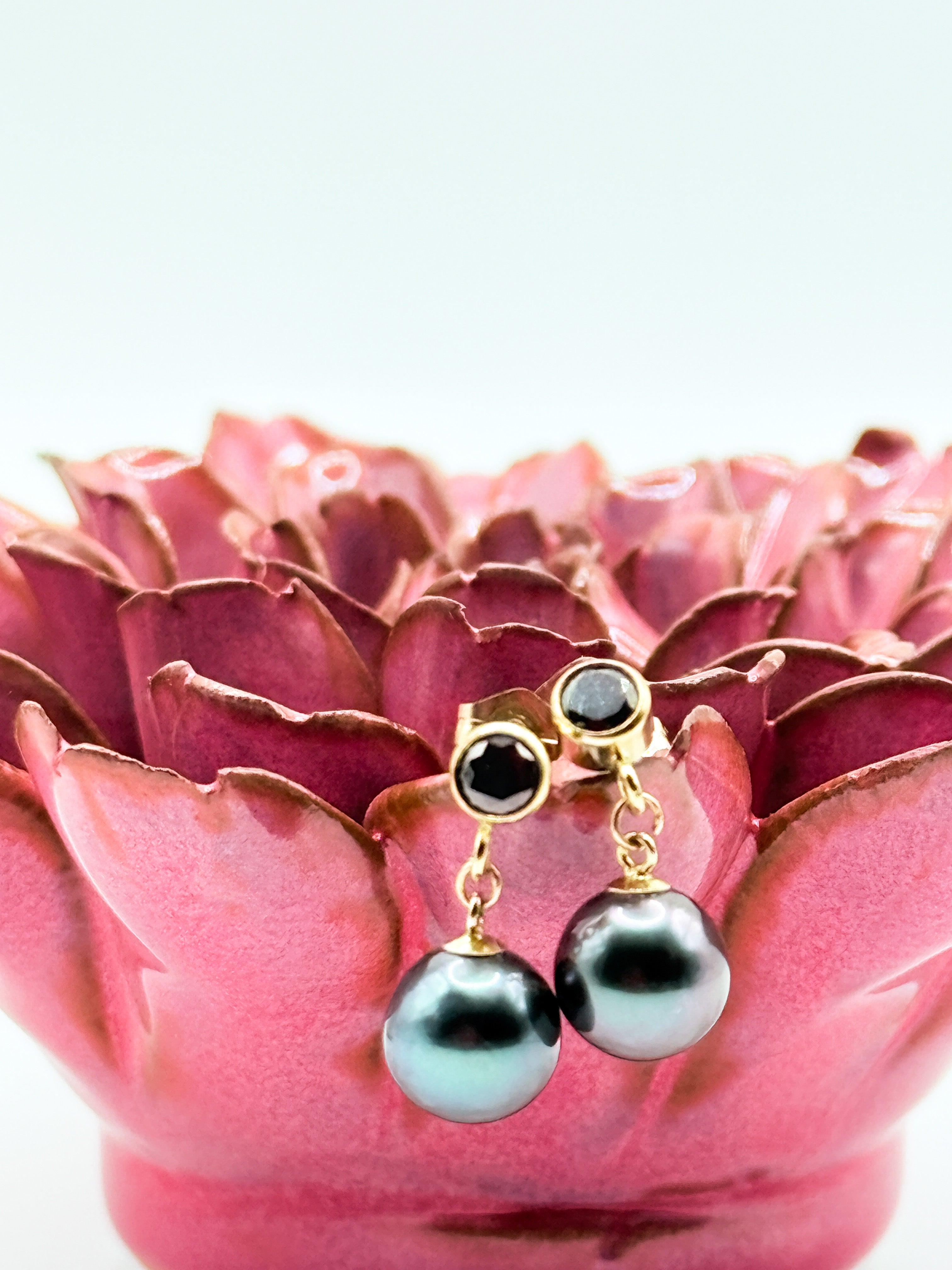 Close-up of earrings resting on white seashell showing dark pearls and faceted black studs